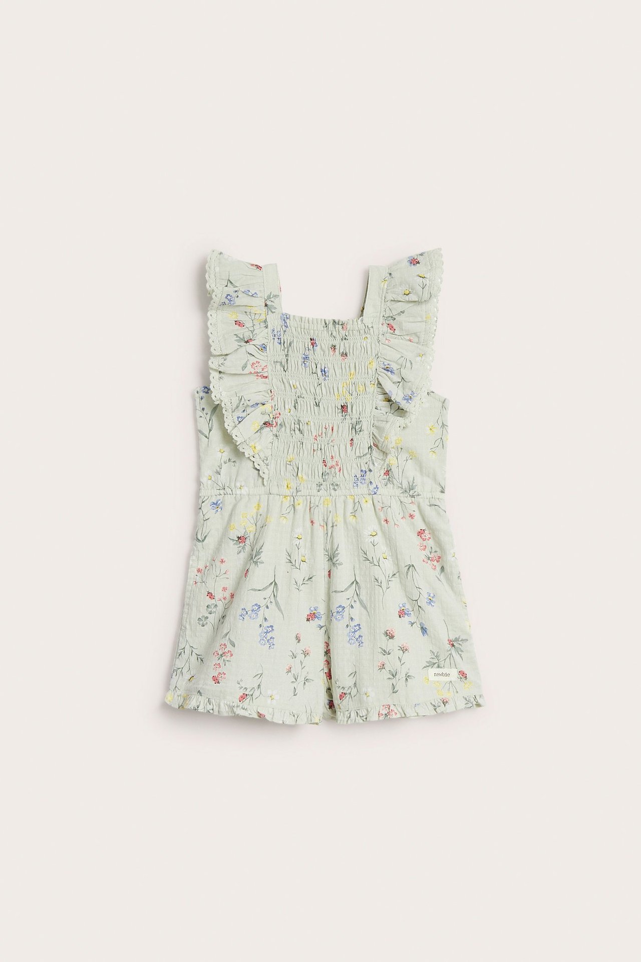 Front view of a kid's light green floral woven romper with ruffled straps and smocked bodice.