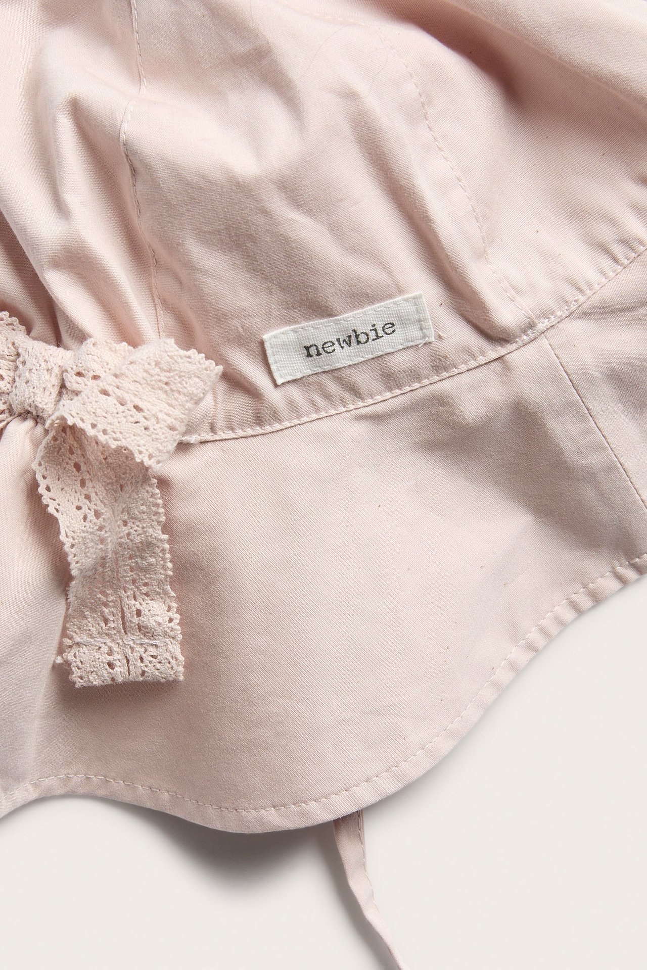 Nahaufnahme eines hellrosa Baumwoll-Sonnenhuts mit längerem Rückenteil, Bindebändern und Spitzenschleife.