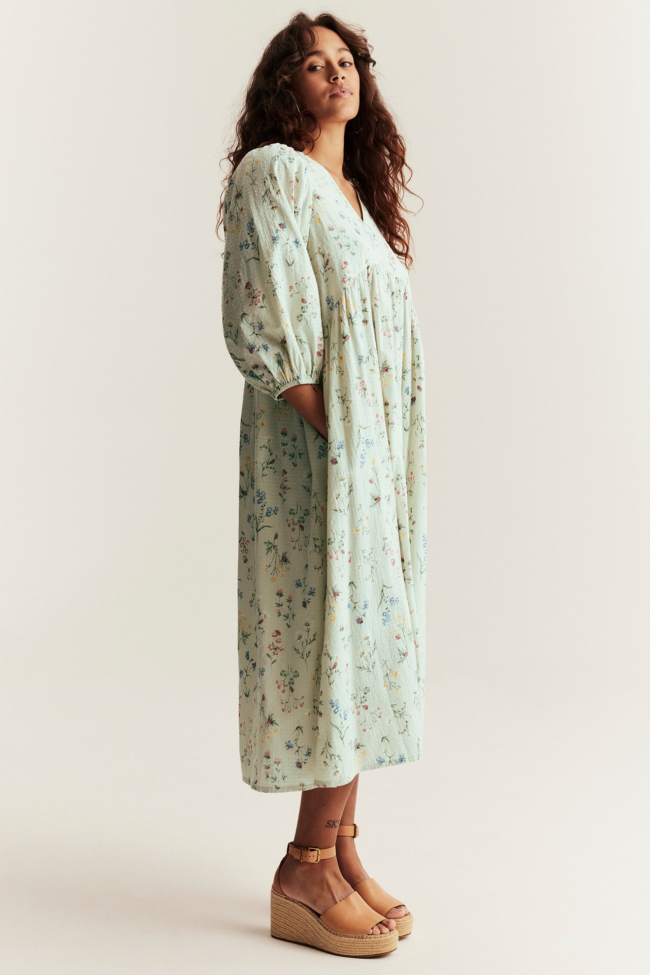 Side view: Woman in light green floral cotton midi dress with puff sleeves and espadrille wedge sandals.