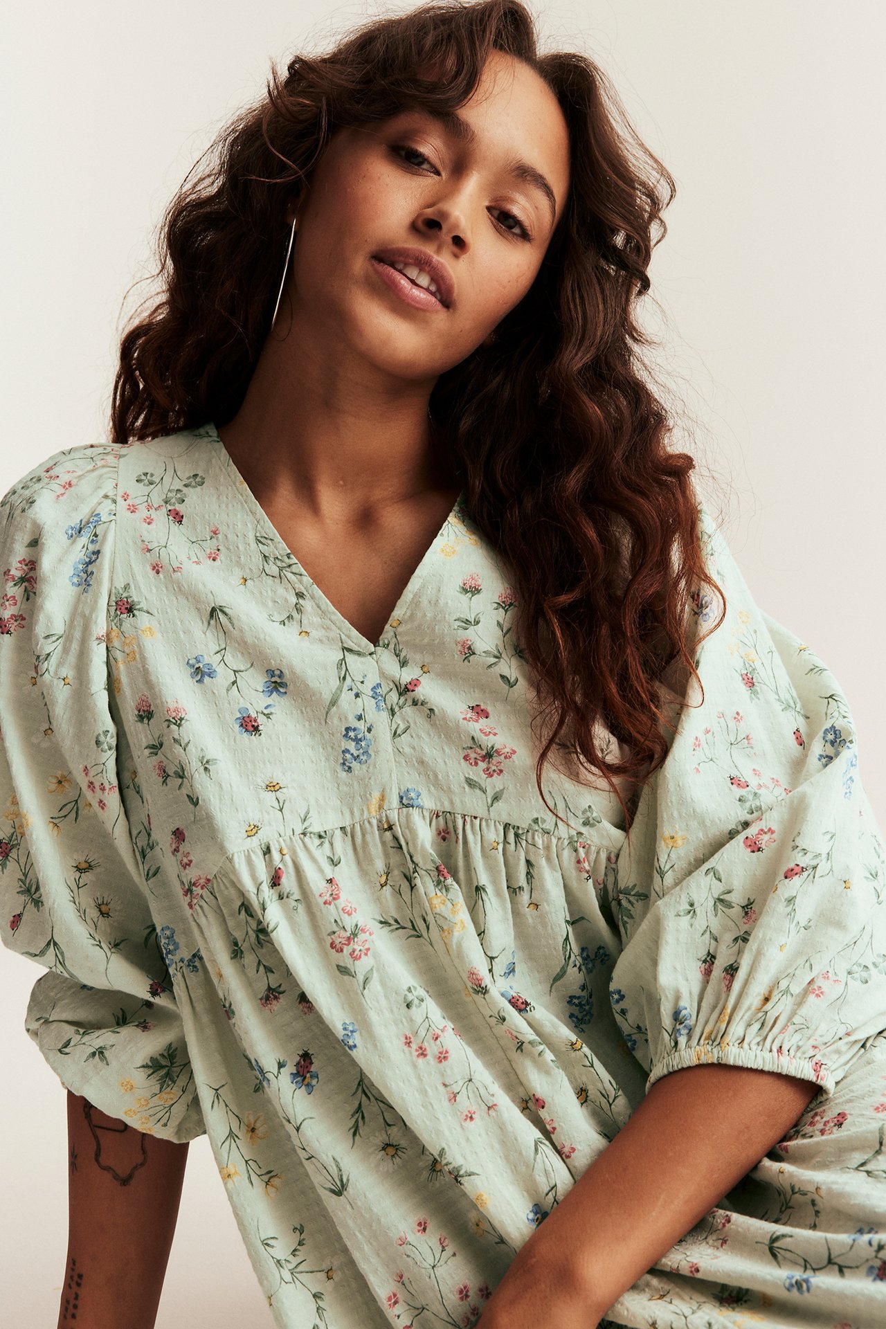 Close-up of a woman in a light green floral cotton V-neck dress with 3/4 length puff sleeves.
