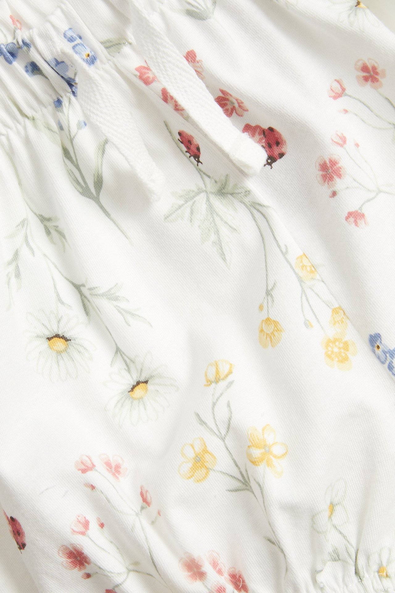 Nahaufnahme von cremeweißen Jersey-Shorts mit Blumen- und Marienkäfermuster, elastischem Kordelzugbund und Rüschen.