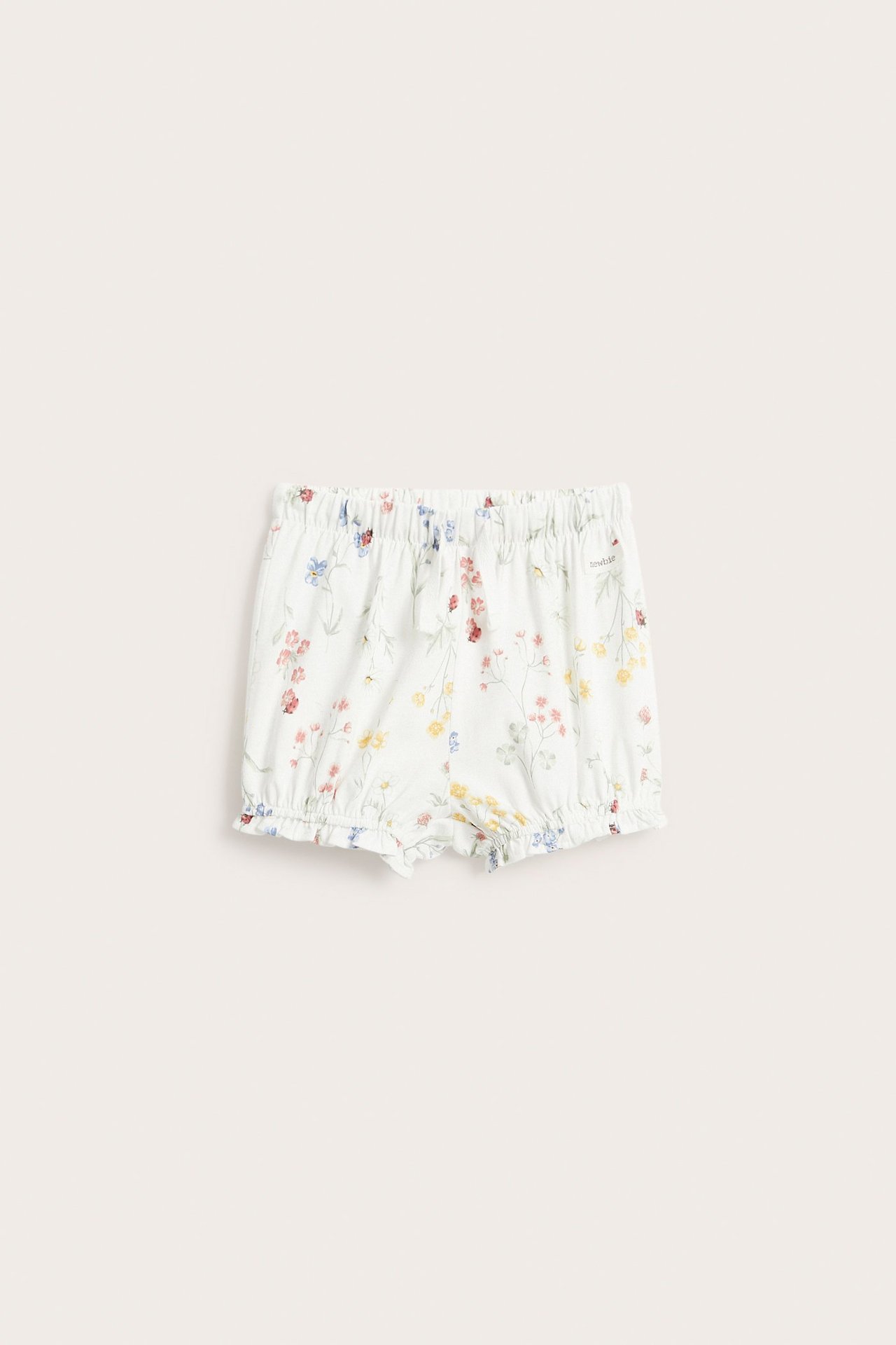 Vorderansicht von cremeweißen Jersey-Shorts für Kinder mit Blumenmuster, elastischem Bund, Kordelzug und Rüschen an den Beinen.