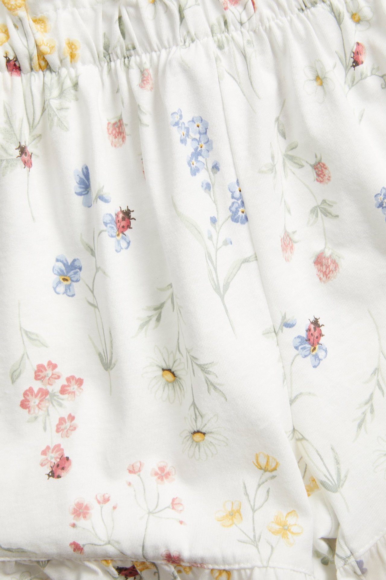 Close-up of off-white cotton jersey shorts with a floral and ladybug print, showing an elasticated waist.