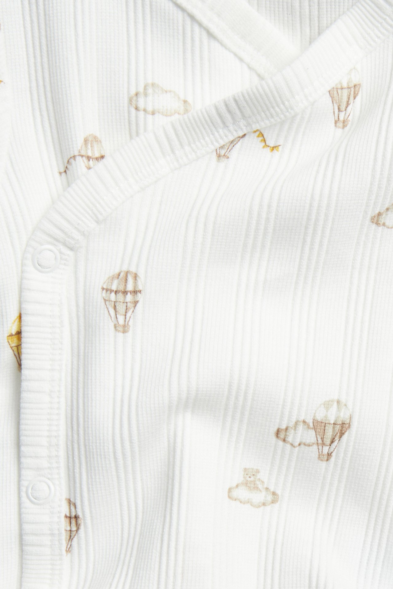 Close-up: Off-white ribbed baby wrap body with snap buttons, printed with hot air balloons and bears.