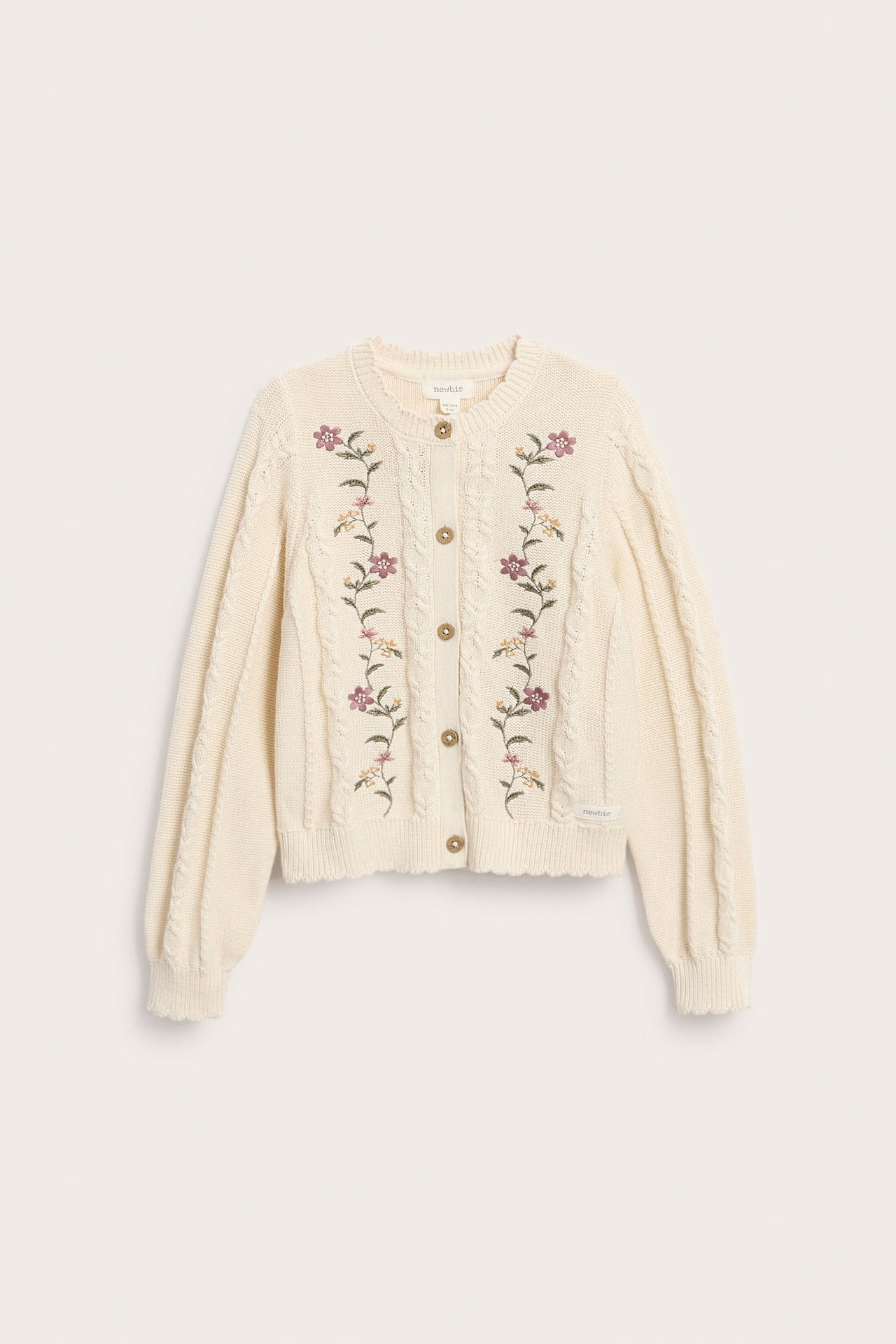 Vorderansicht einer cremefarbenen Zopfmuster-Strickjacke mit Blumenstickerei und braunen Knöpfen.