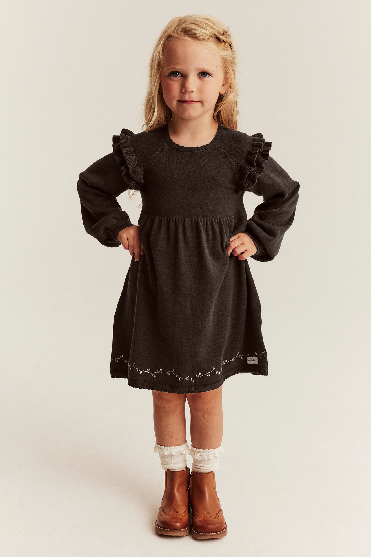 Vorderansicht: Kind in dunkelgrauem Rüschenkleid mit weißer Stickerei, Socken, braunen Lederstiefeln.