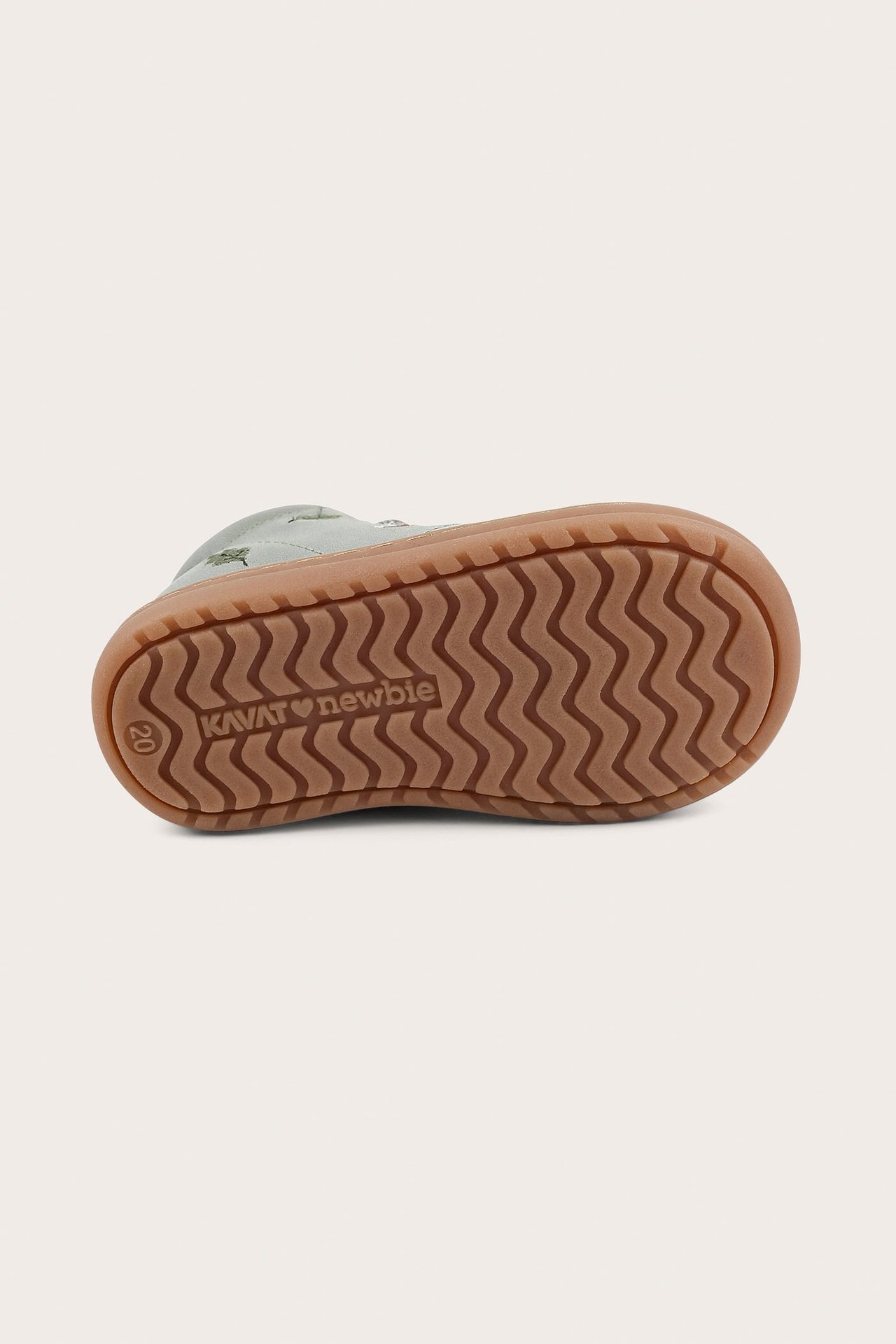 Close-up bottom view of a kid's green patterned learn-to-walk shoe with a brown rubber sole.