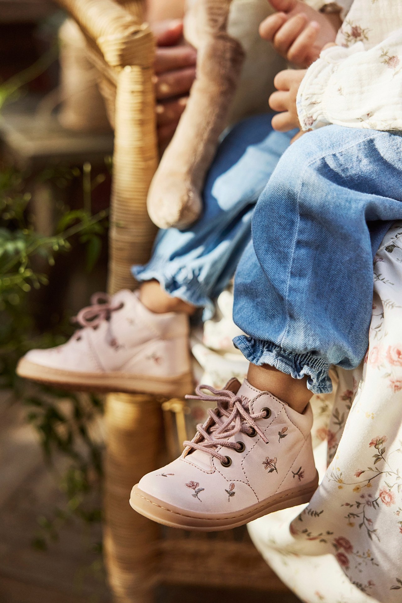 Close-up: baby wears light pink floral leather walking shoes, blue ruffled denim pants.