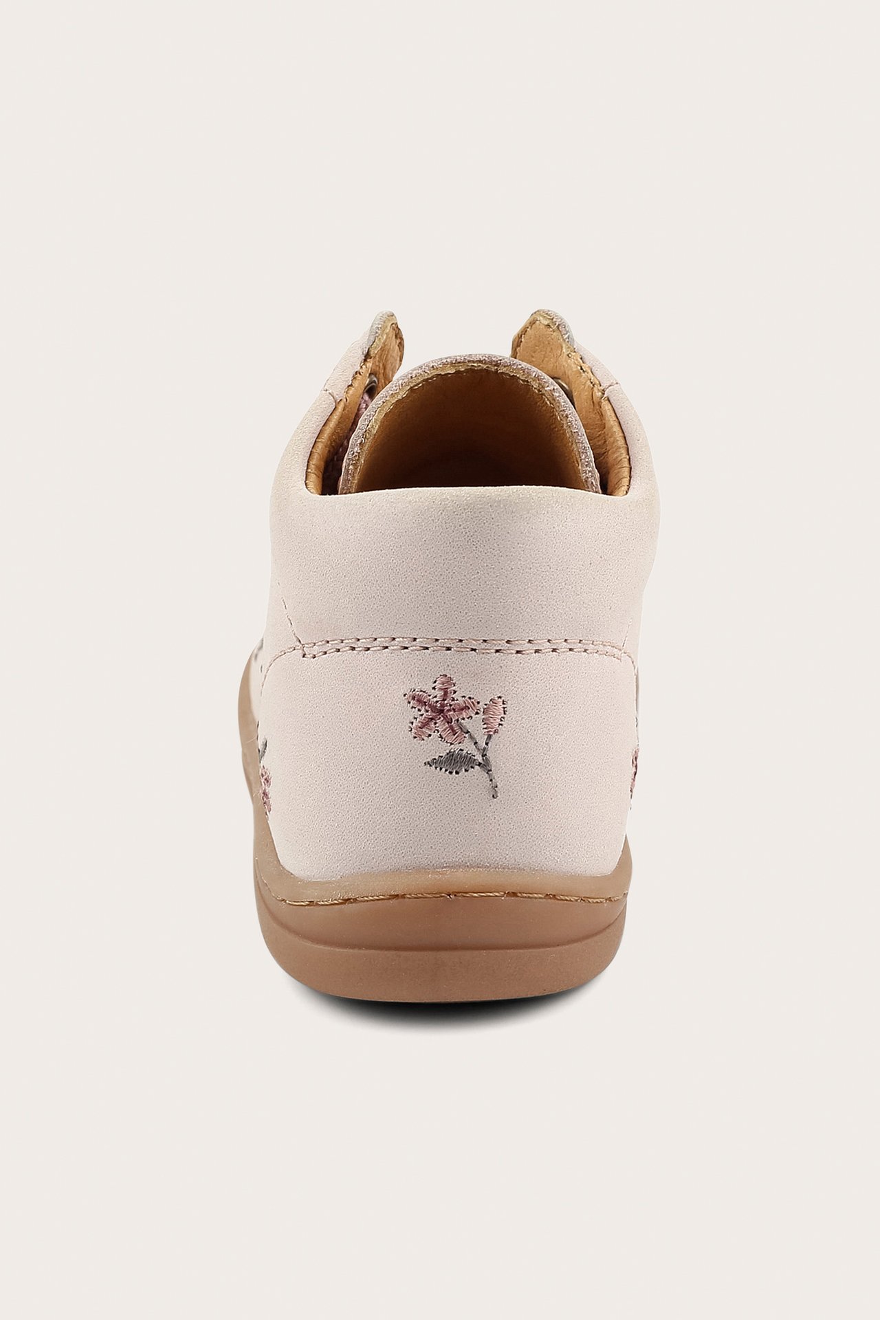 Rear view of a light pink kid's learn-to-walk shoe with small pink floral embroidery and a brown sole.