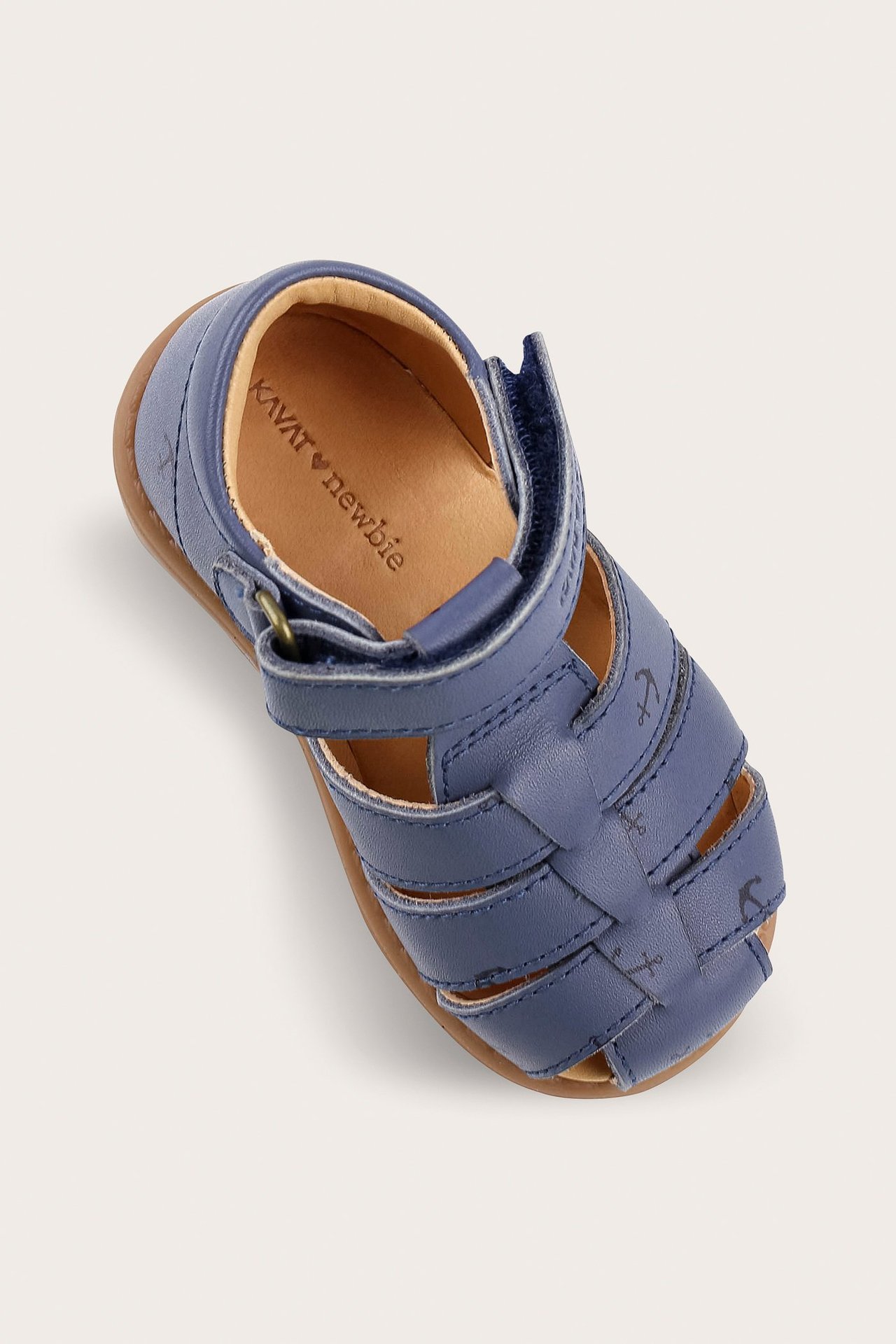 Top-down view of a blue leather baby sandal with a closed toe, anchor print, and velcro strap.