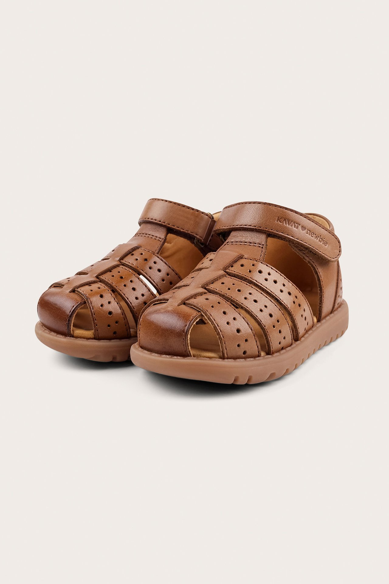 Angled front view of brown leather kid's sandals with closed perforated toes and hook-and-loop straps.
