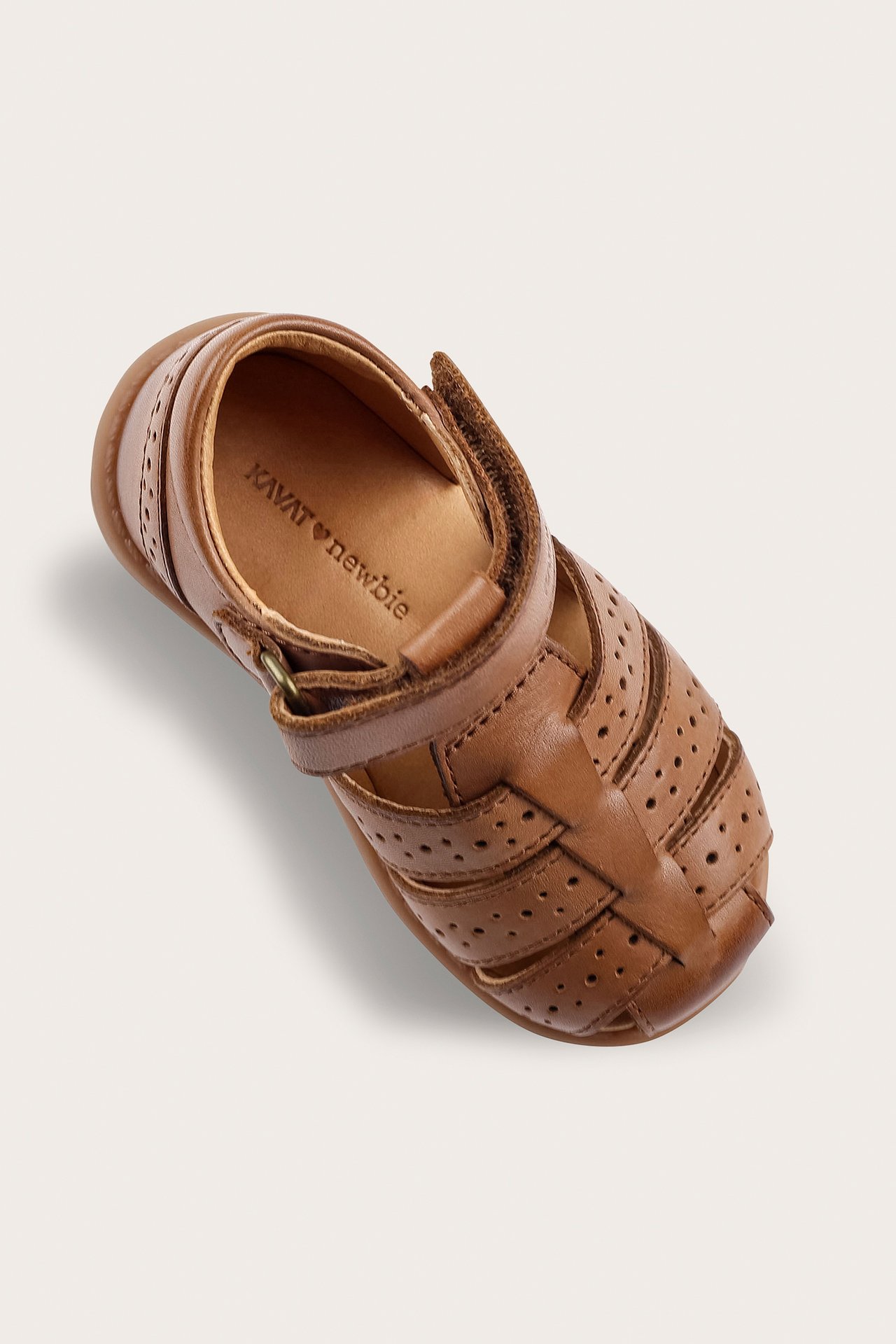 High-angle view of a brown leather kid's closed-toe sandal with perforated details and velcro strap.