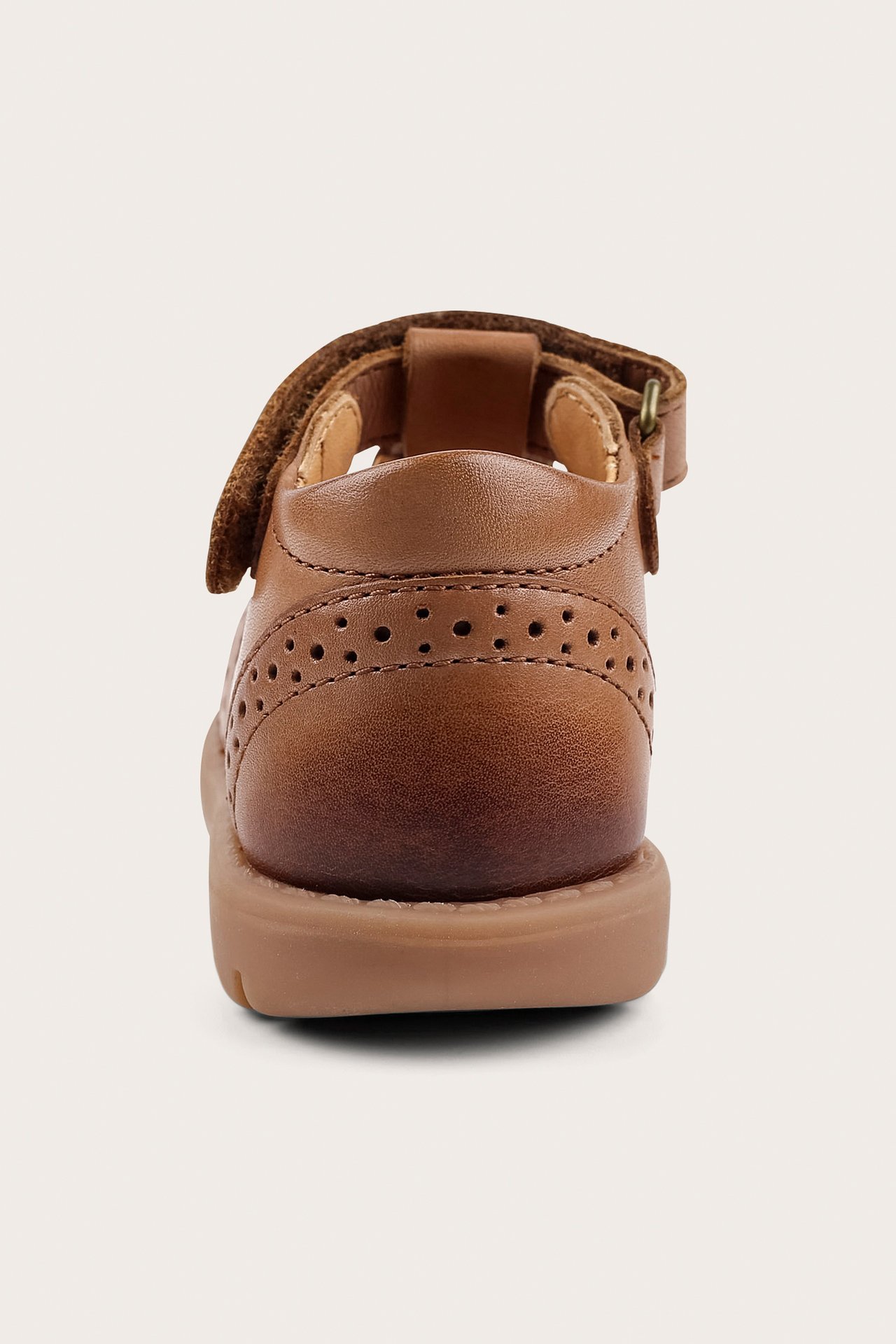 Close-up back view of a kid's brown leather sandal with perforated details and an ankle buckle strap.