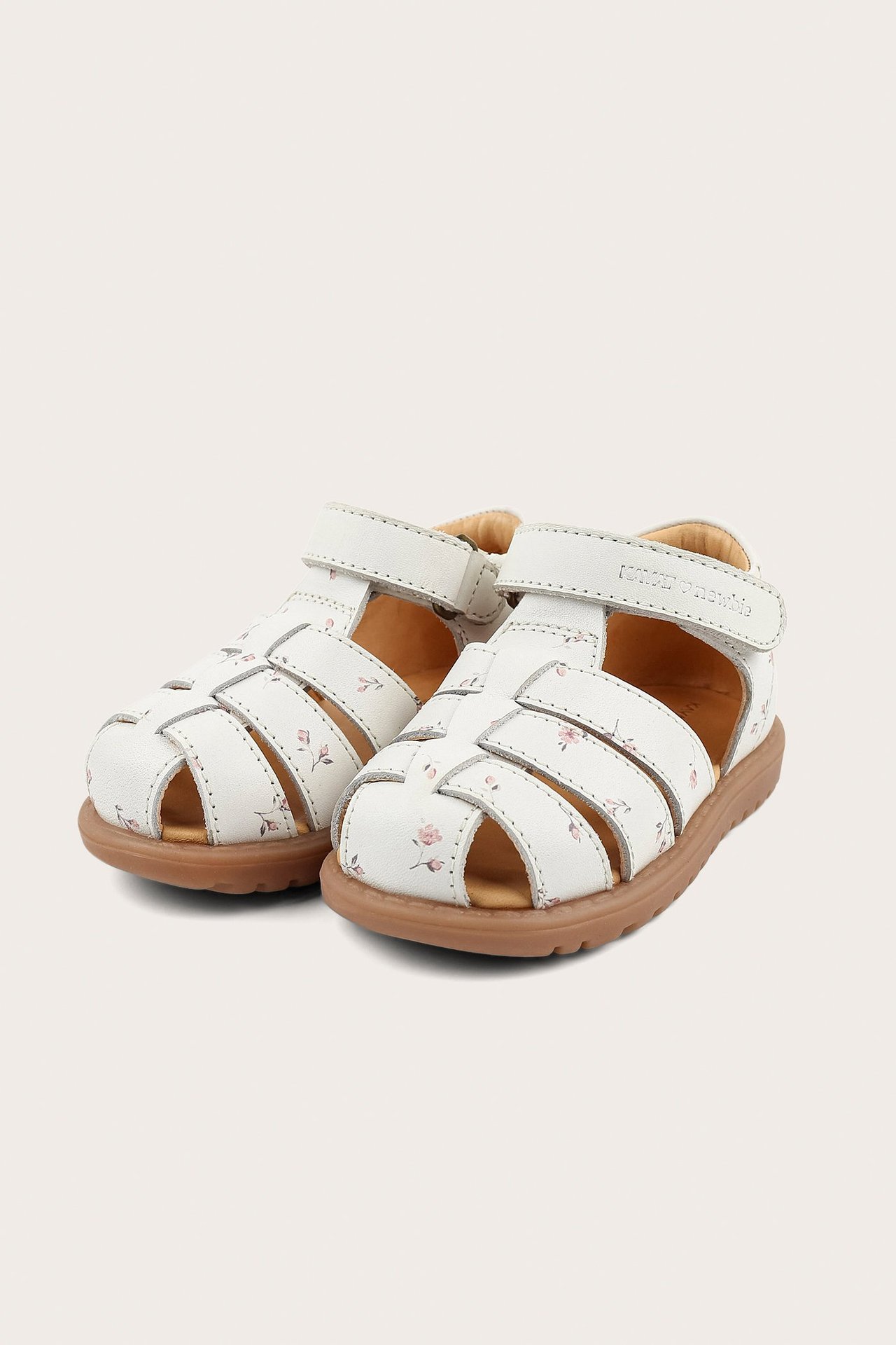 Front view of white kid's sandals with pink floral pattern, brown soles, and Velcro straps.