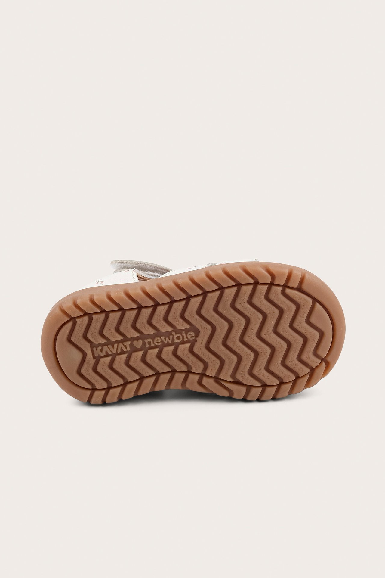 Bottom view of a kid's white floral sandal with a prominent wavy brown rubber sole.