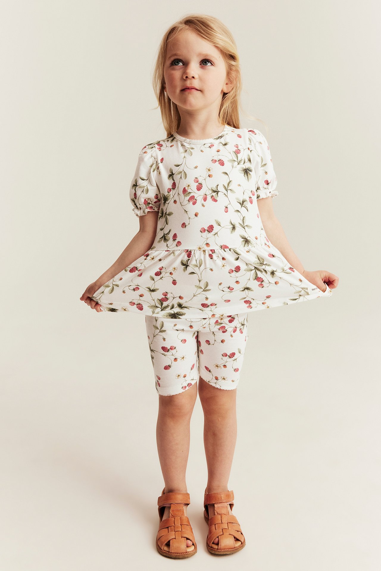 Vorderansicht Kind: cremeweißes Peplum-Top mit Erdbeermuster, passende Shorts, braune Sandalen.