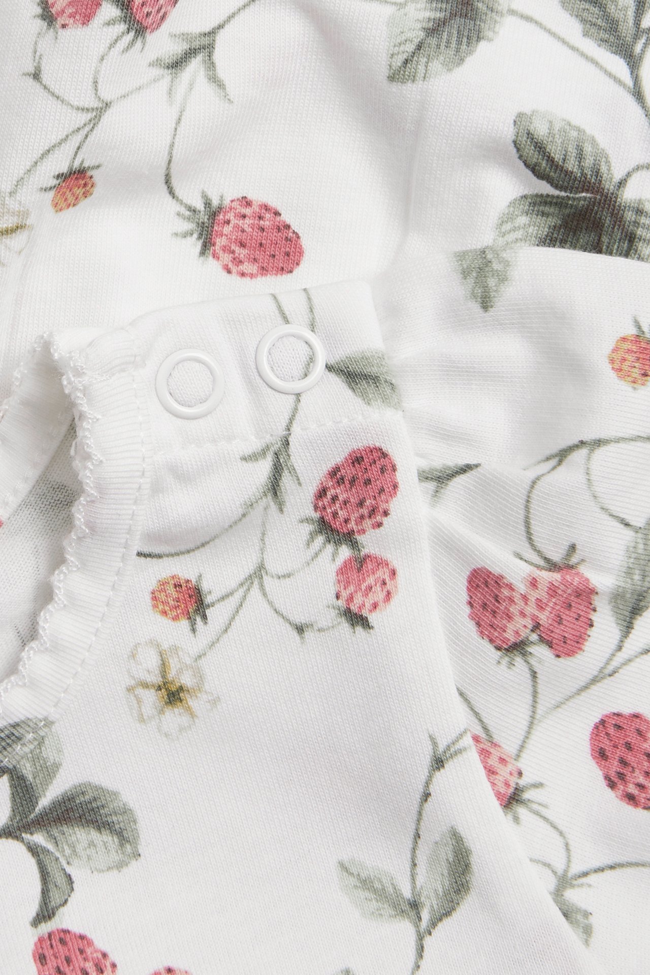 Nahaufnahme: Cremeweißes Baumwoll-Jersey-Peplum-Oberteil mit rosa Erdbeermuster und weißen Druckknöpfen.