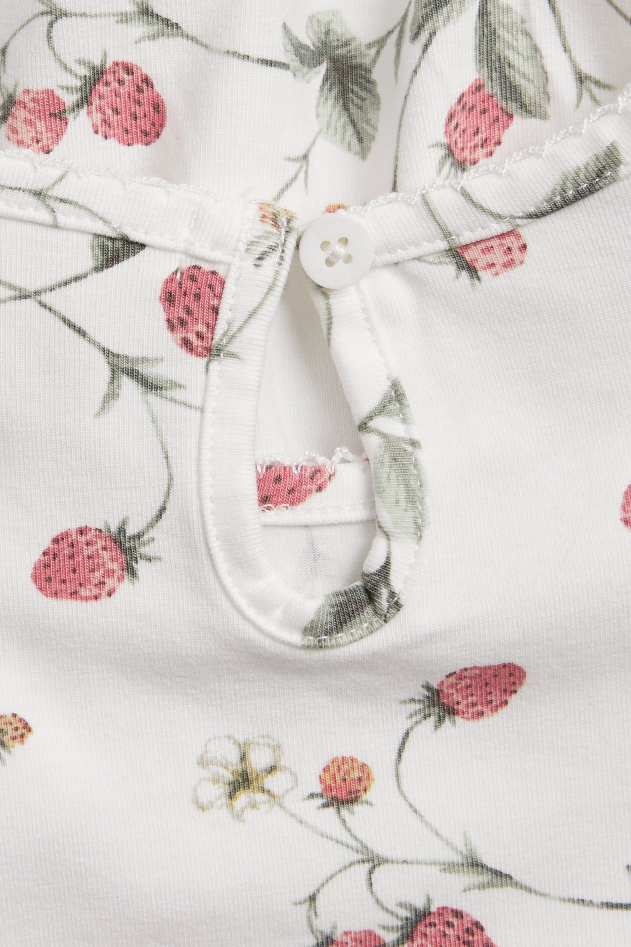 Nahaufnahme Rückansicht eines cremefarbenen Jersey-Tops mit Erdbeermuster, Knopf und Gummischlaufe.