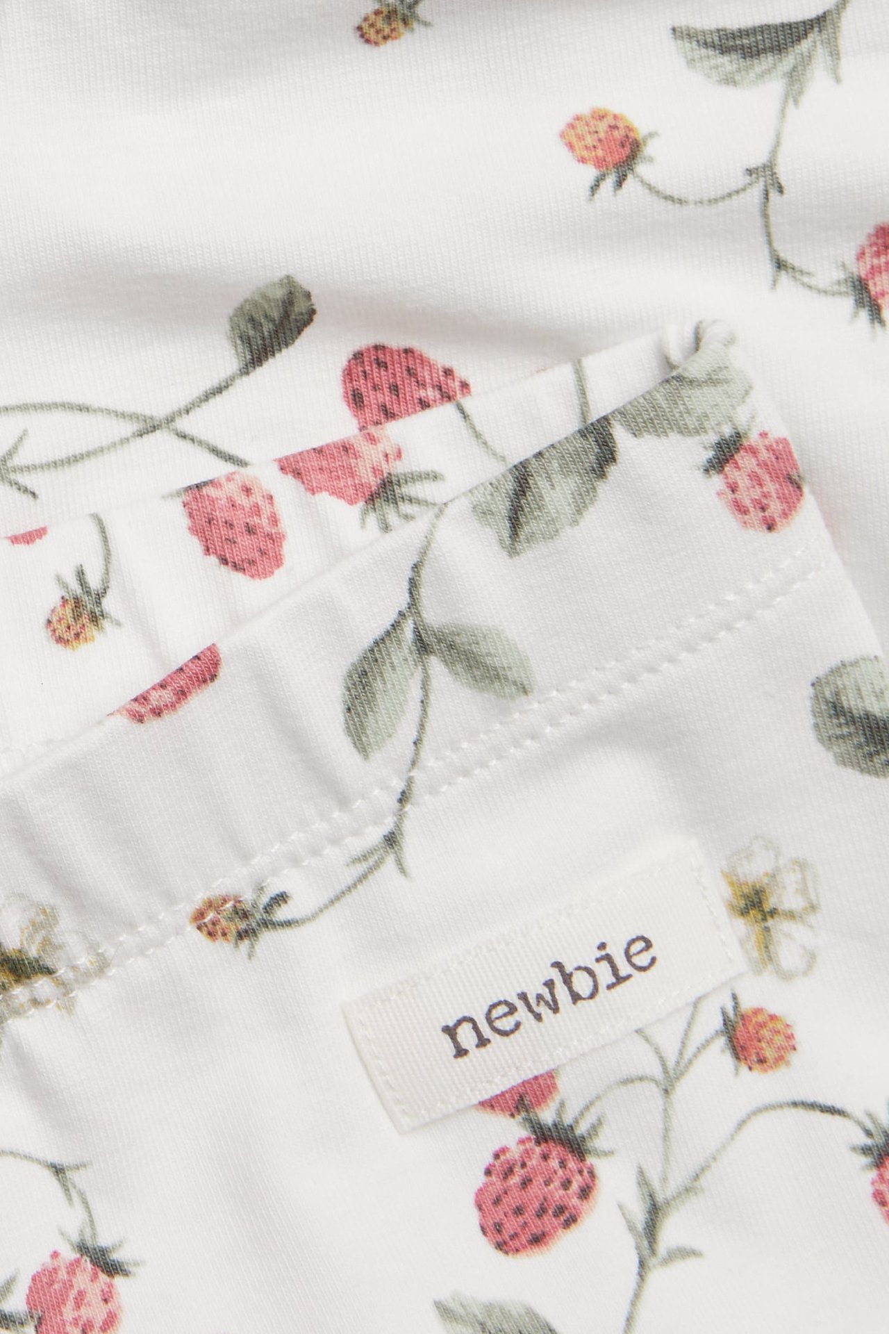 Nahaufnahme von cremefarbenen Jersey-Leggings mit rotem Erdbeermuster und sichtbarem 'newbie'-Etikett.