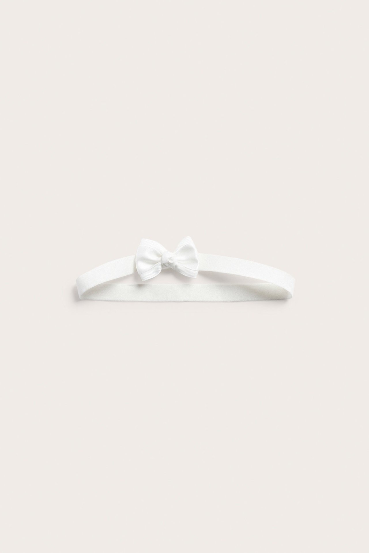 Front view of an off-white elastic headband with a small satin bow.