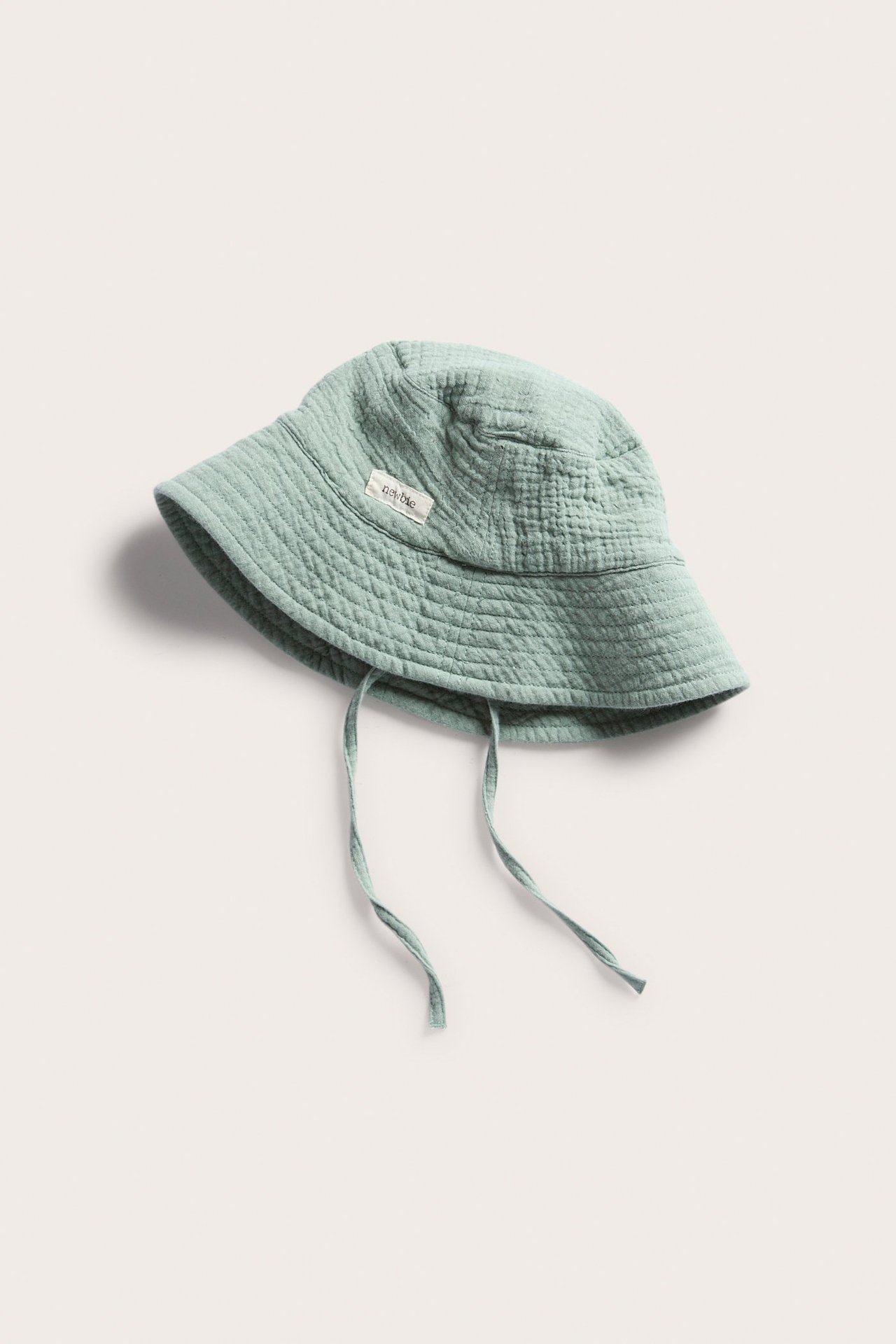 Hochwinkelansicht eines einfarbigen grünen Baby-Sonnenhuts mit Bindebändern, aus weichem, gestepptem Stoff.