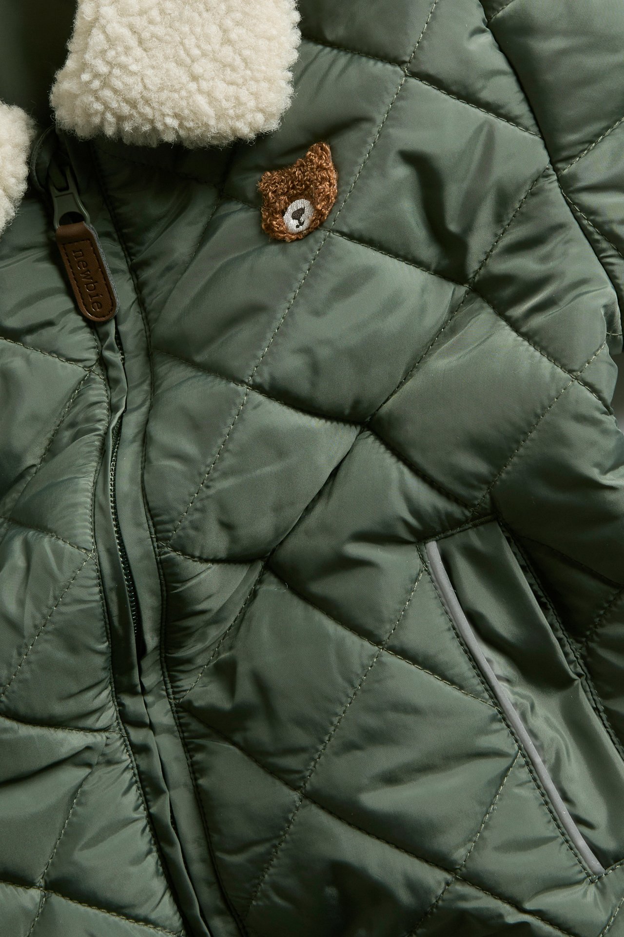 Front view: dark green quilted kid's jacket with cream pile collar and teddy bear embroidery.