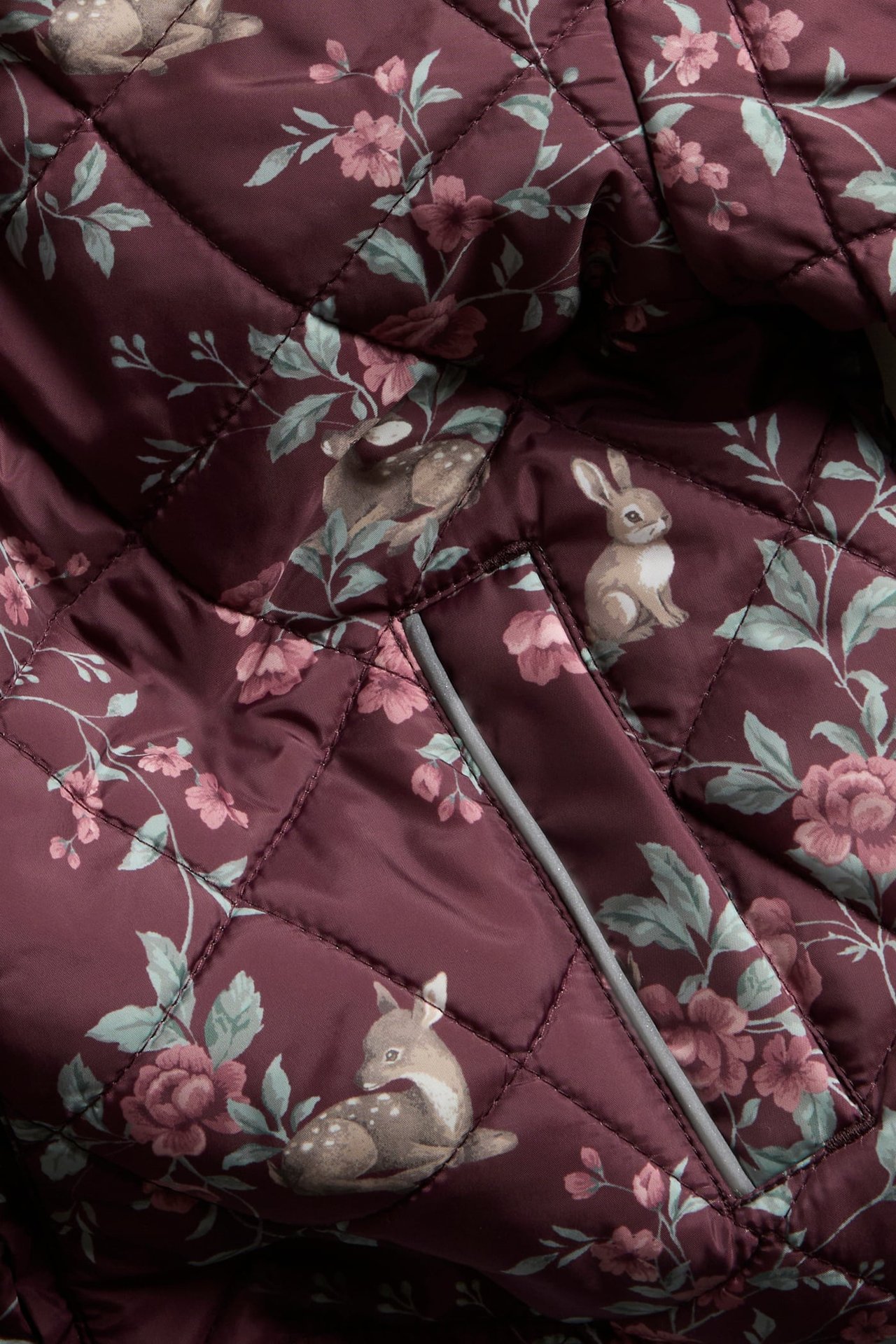 Nahaufnahme einer weinroten Steppjacke mit Blumen-, Reh- und Kaninchenmuster und Reflexdetail.