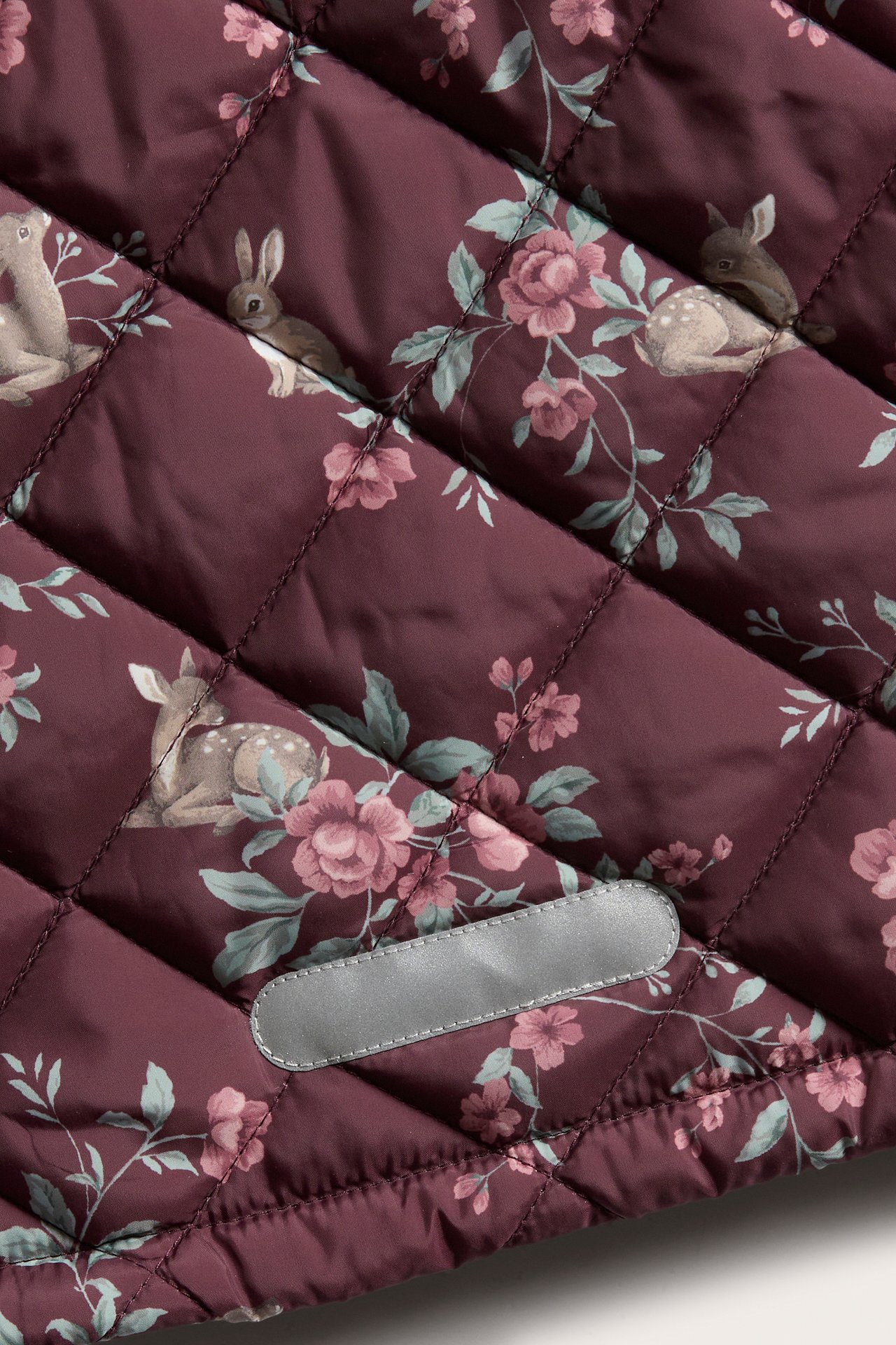 Close-up of a quilted wine red jacket with floral, deer, and rabbit print, featuring a reflective detail.