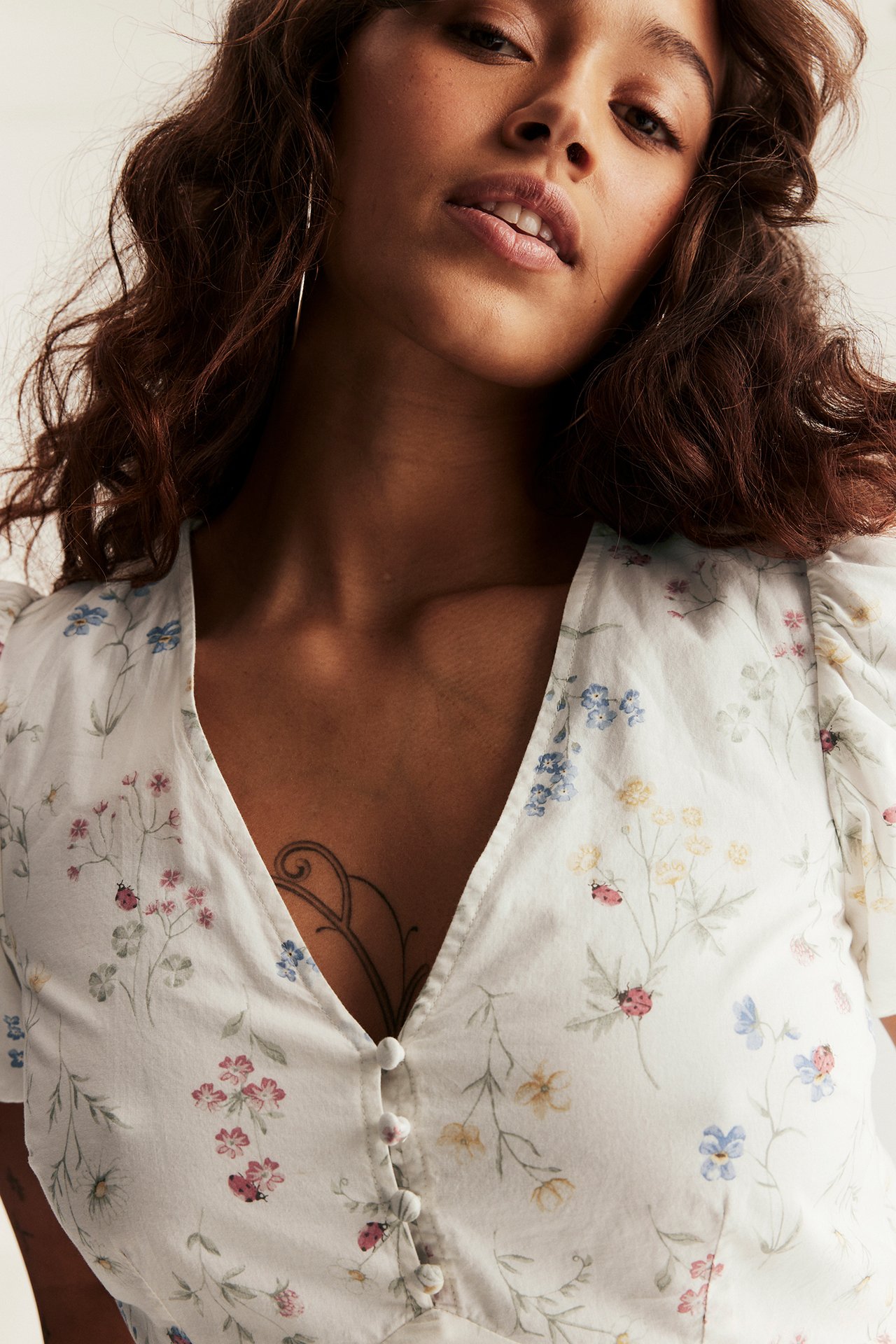 Woman in offwhite floral V-neck dress with covered buttons and puff sleeves, wearing hoop earrings.