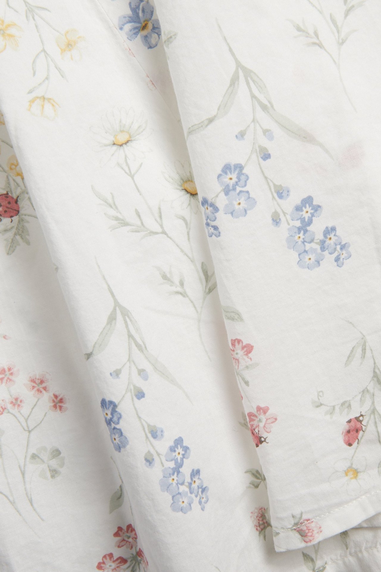 Close-up of off-white cotton fabric with a small floral pattern, featuring blue, yellow, pink flowers, and ladybugs.