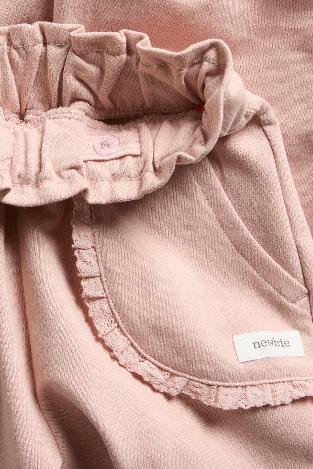 Close-up of pink cotton jogging pants with adjustable elastic waist and lace-trimmed pocket.