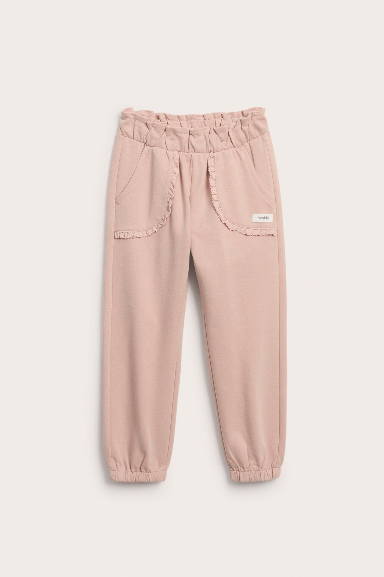 Front view of kid's solid pink cotton jogging pants with ruffled elastic waist and lace-trimmed front pockets.