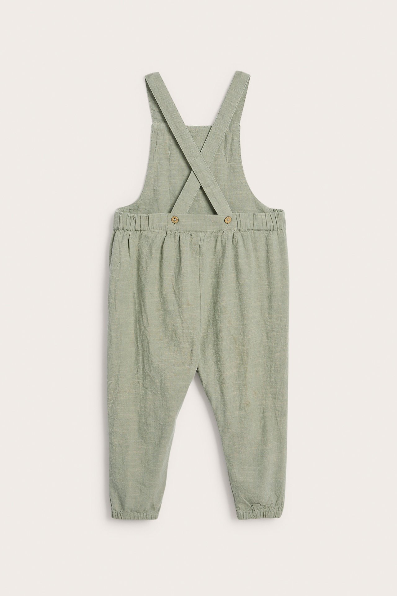 Back view of dark green woven baby overalls with adjustable cross-back straps and elasticated cuffs.
