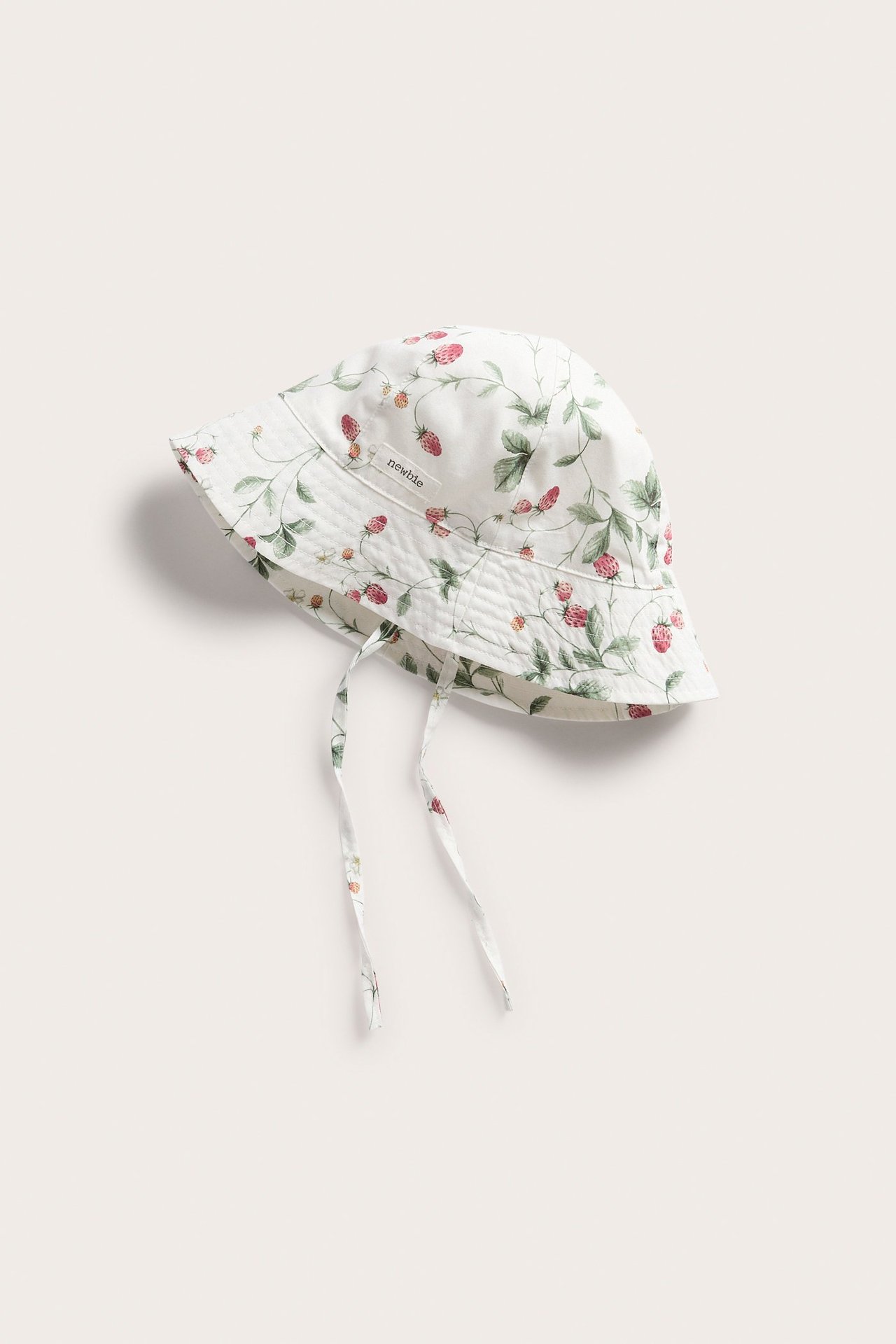 Ansicht von oben: Ein cremefarbener Baumwoll-Sonnenhut mit rotem Erdbeermuster und Bindebändern.