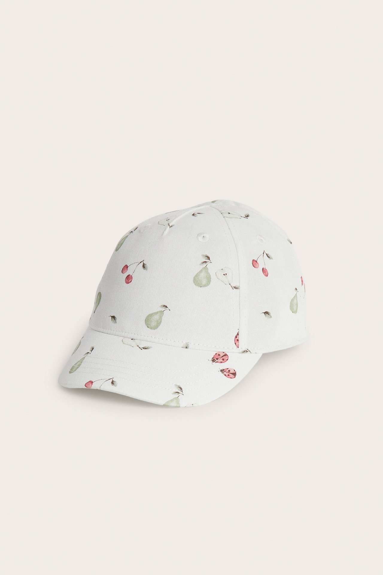 Front-side view of an off-white cap patterned with green pears, red cherries, and ladybugs.