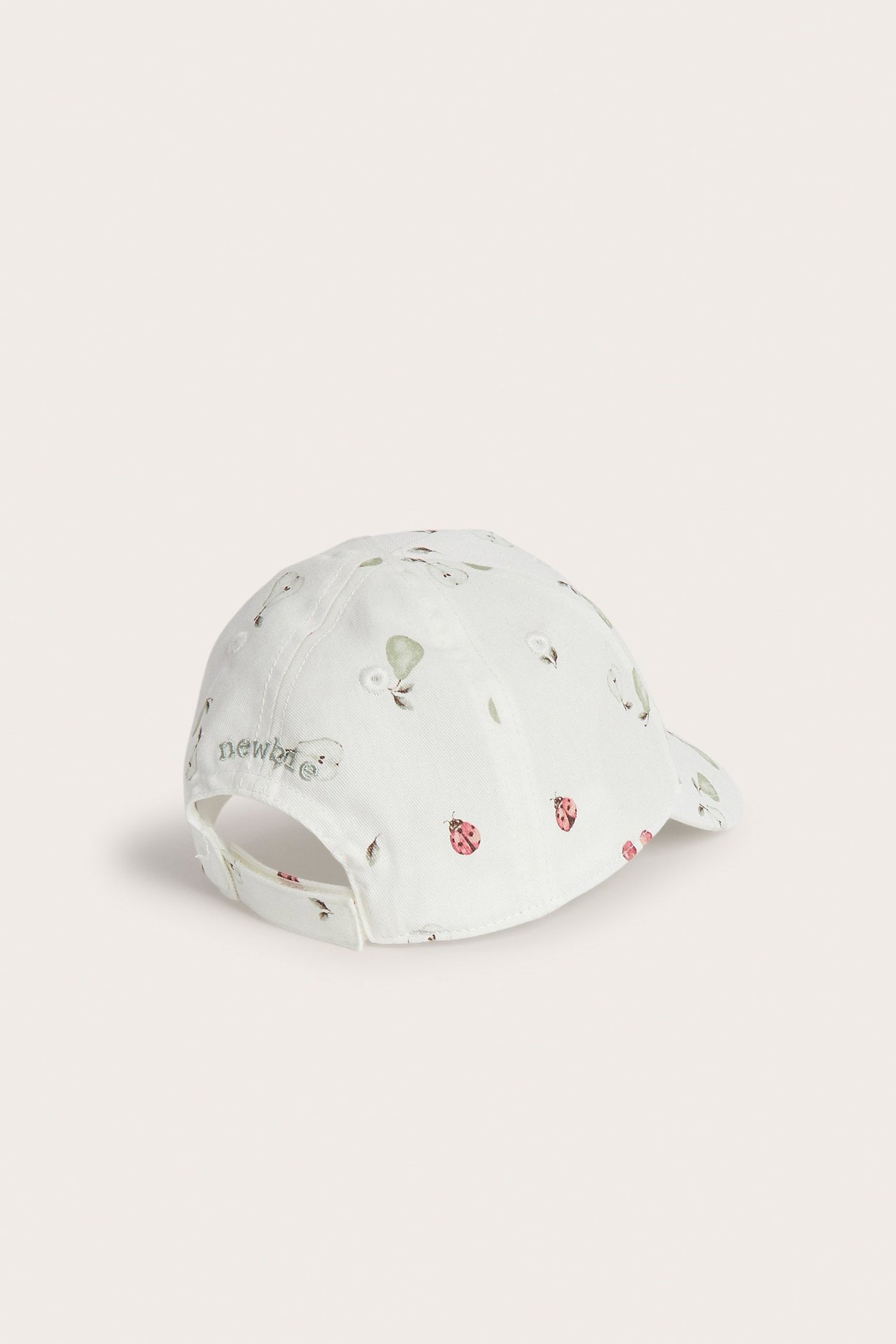 Back view of an offwhite kid's cap with fruit and ladybug pattern, velcro-adjustable with Newbie embroidery.