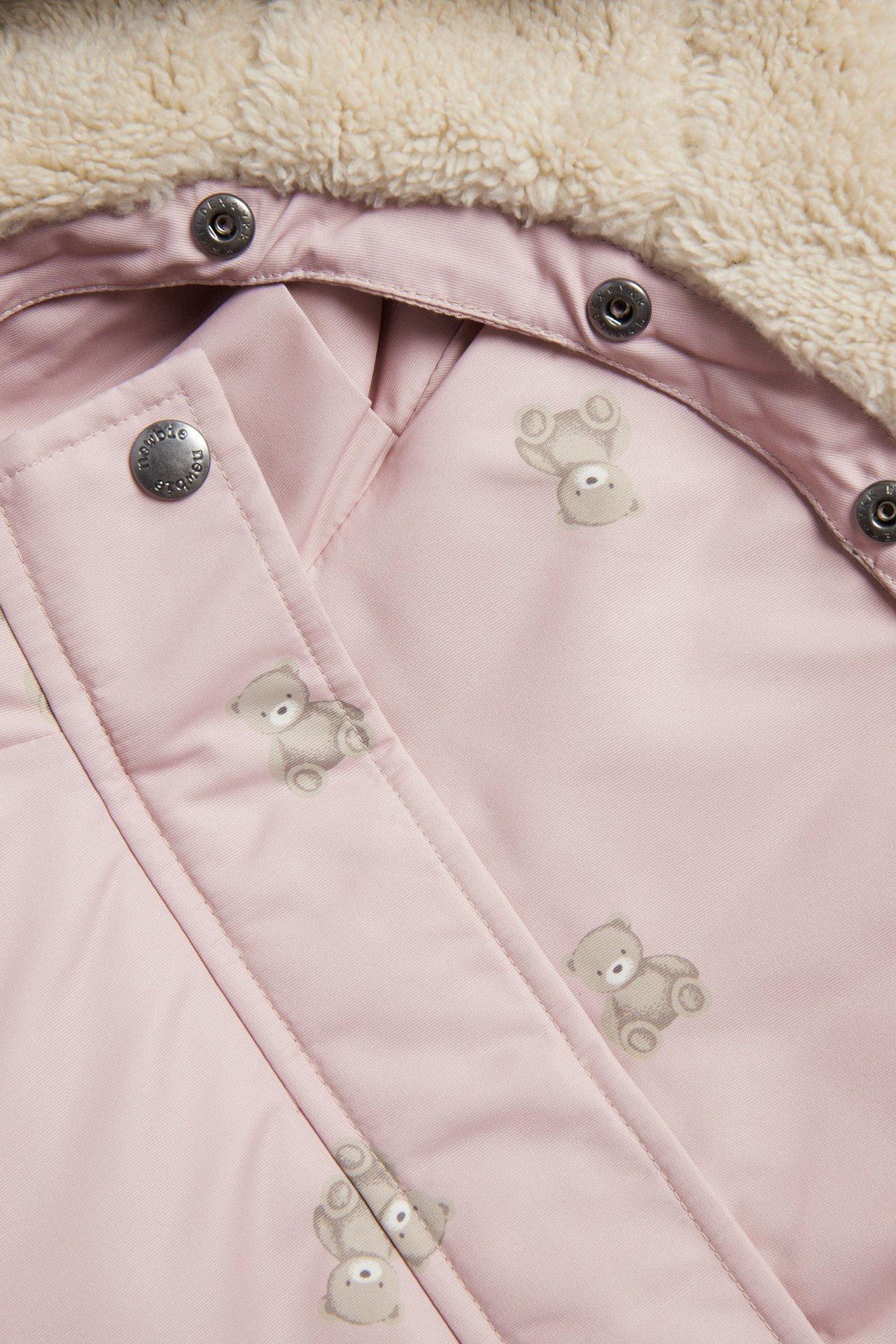 Close-up of a pink baby jacket with teddy bear print, cream fuzzy lining and silver snaps.