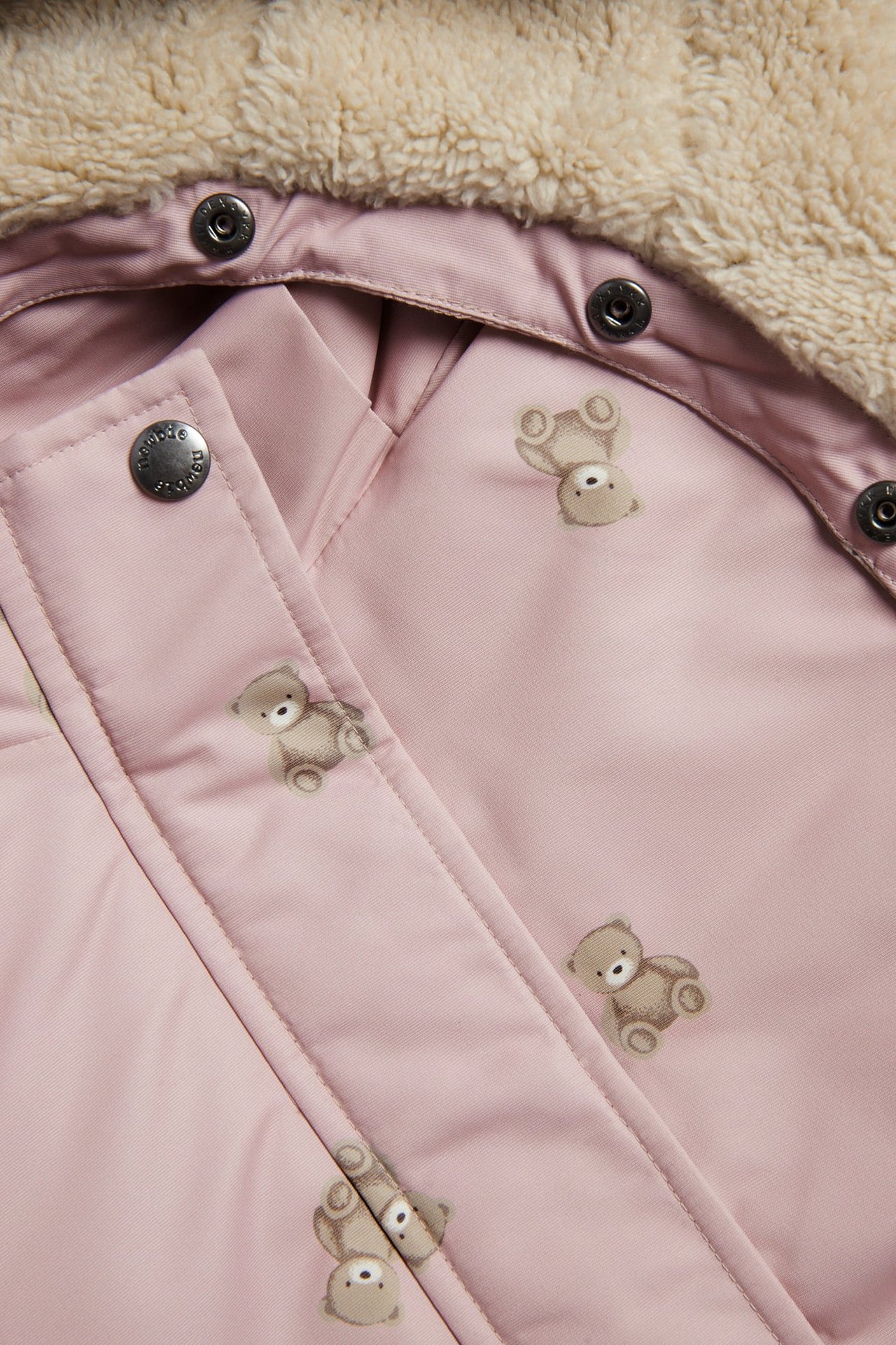 Nahaufnahme einer rosa Babyjacke mit Teddybärenmuster und flauschigem Futter, Druckknöpfe.