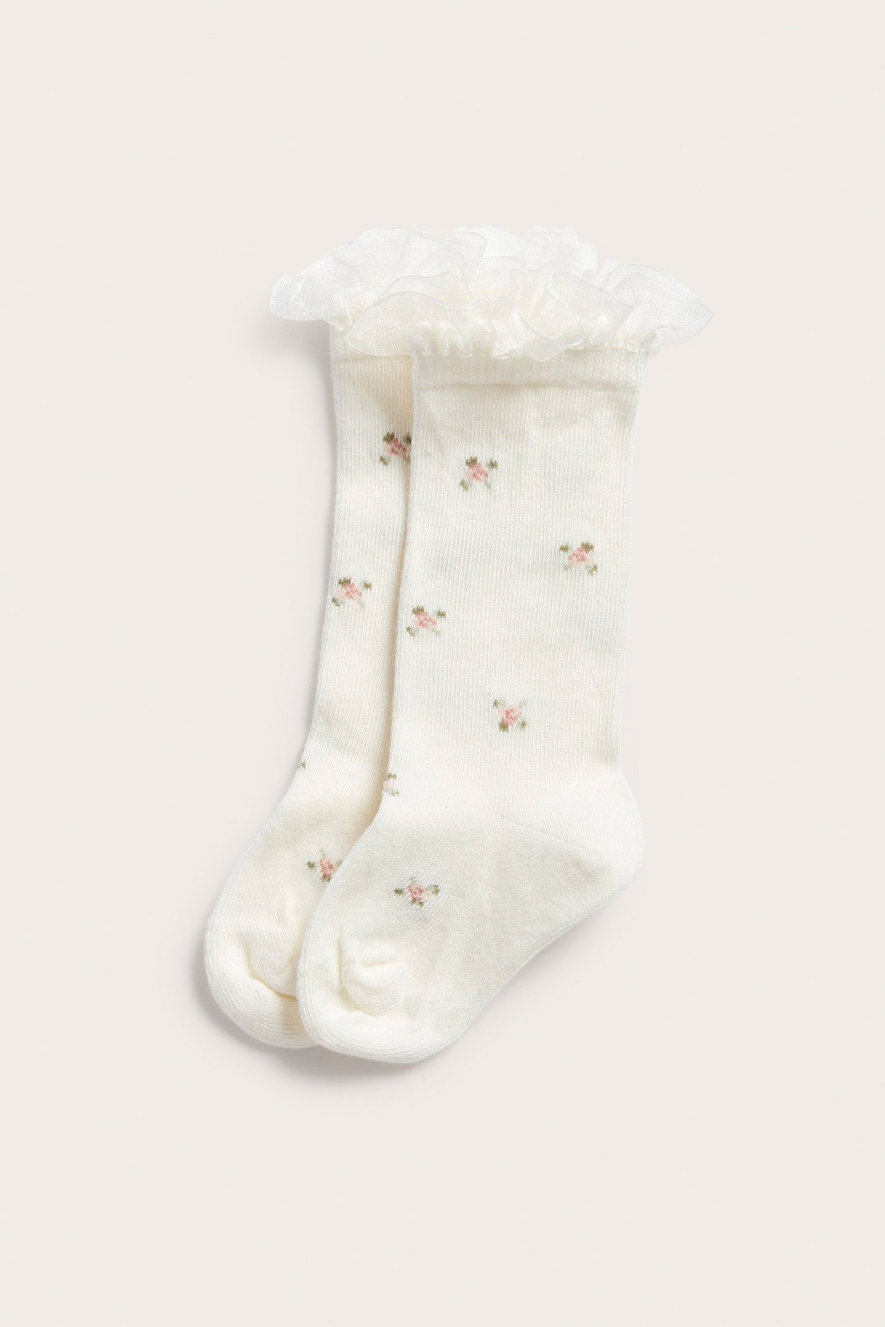 Front view of off-white knee-high socks with small floral print and a shimmering ruffled top.