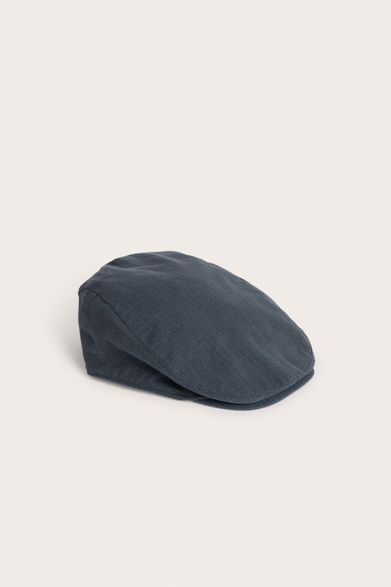 Side view of a dark blue textured woven flat cap with Newbie embroidery and elastic at the back.