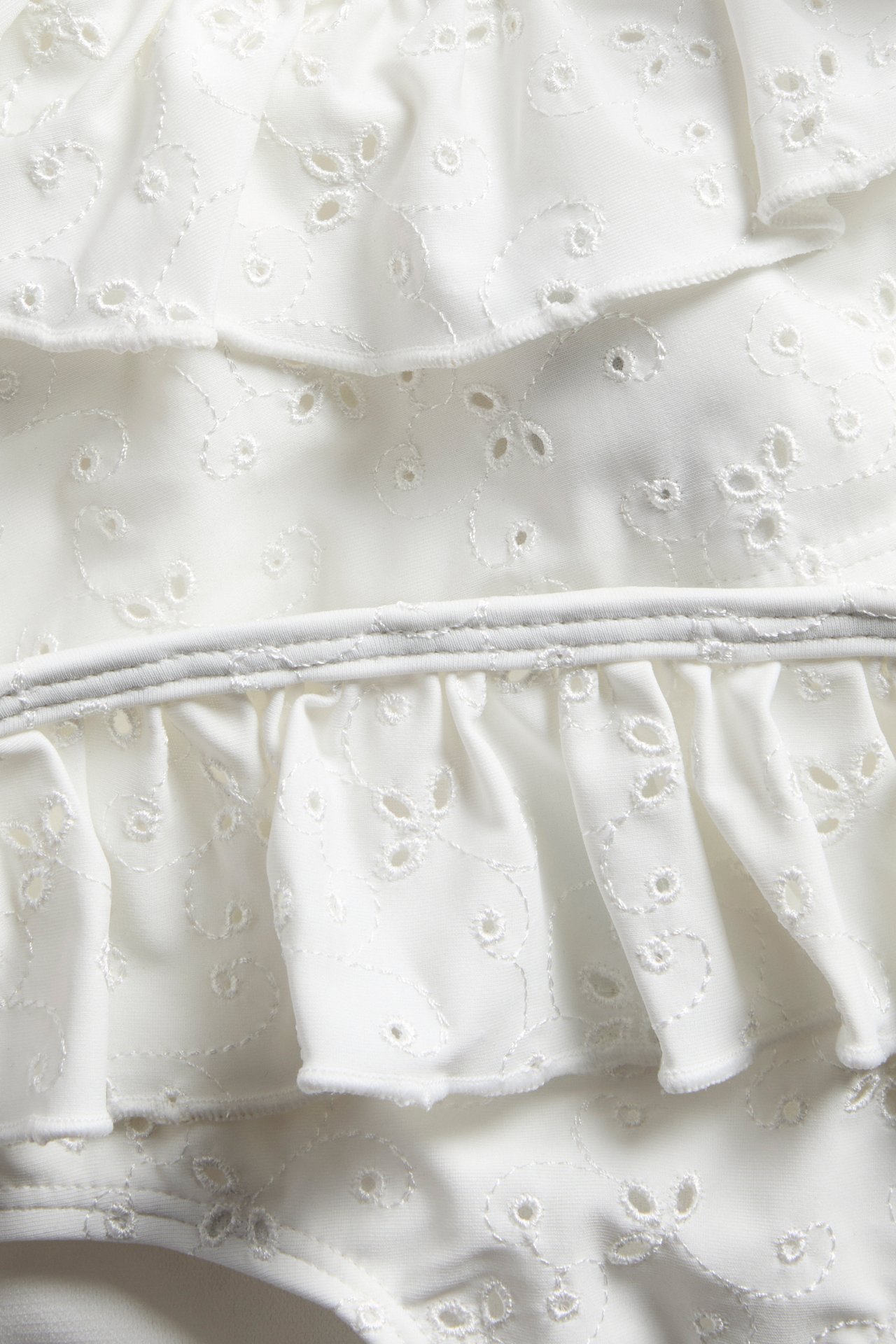 Nahaufnahme eines off-white Bikinis mit Rüschen und einem durchgehenden gestickten Lochmuster.