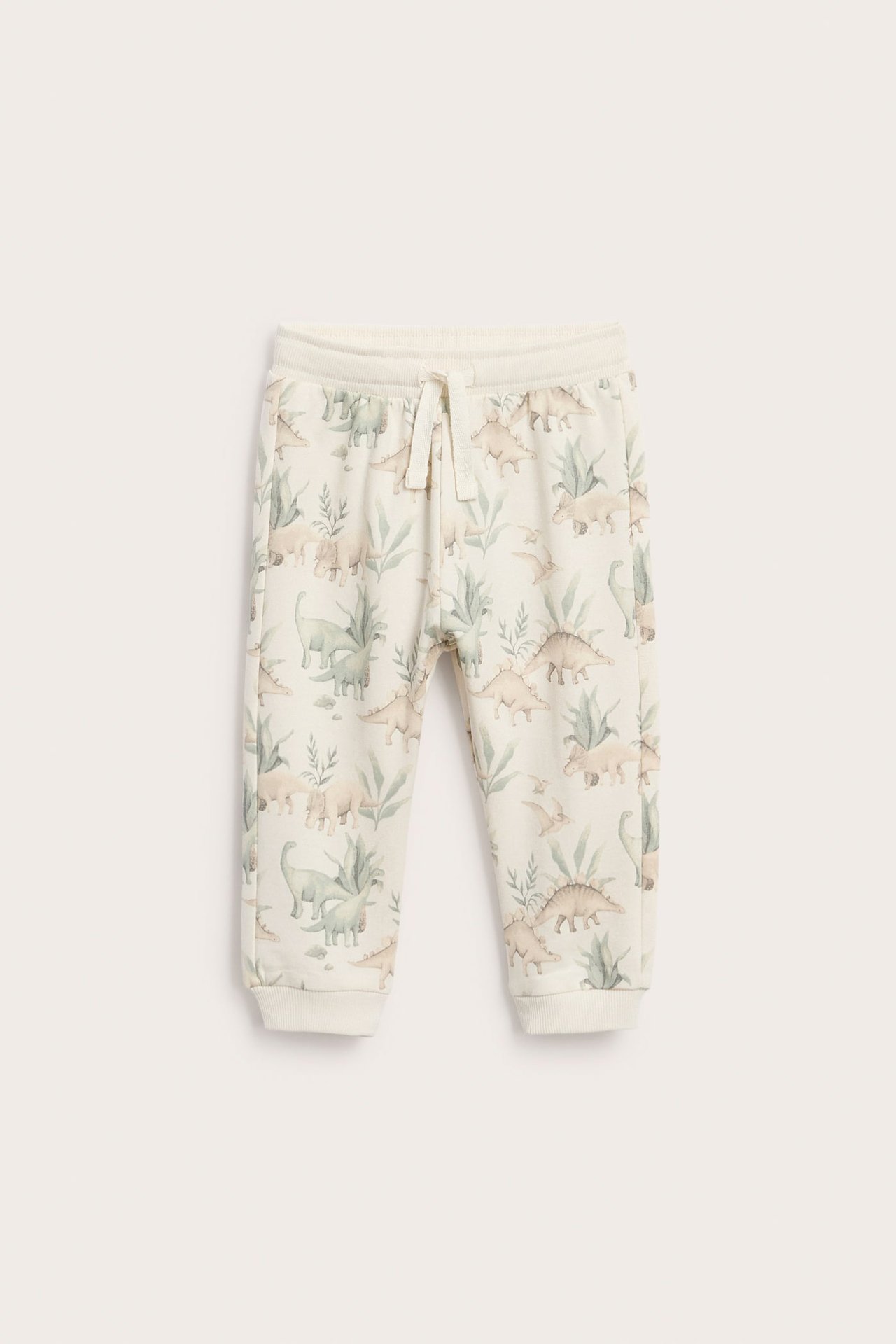 Vorderansicht: Baby-Jogginghose in Creme mit Dinosaurier- und Pflanzenmuster, Kordelzug und Bündchen.