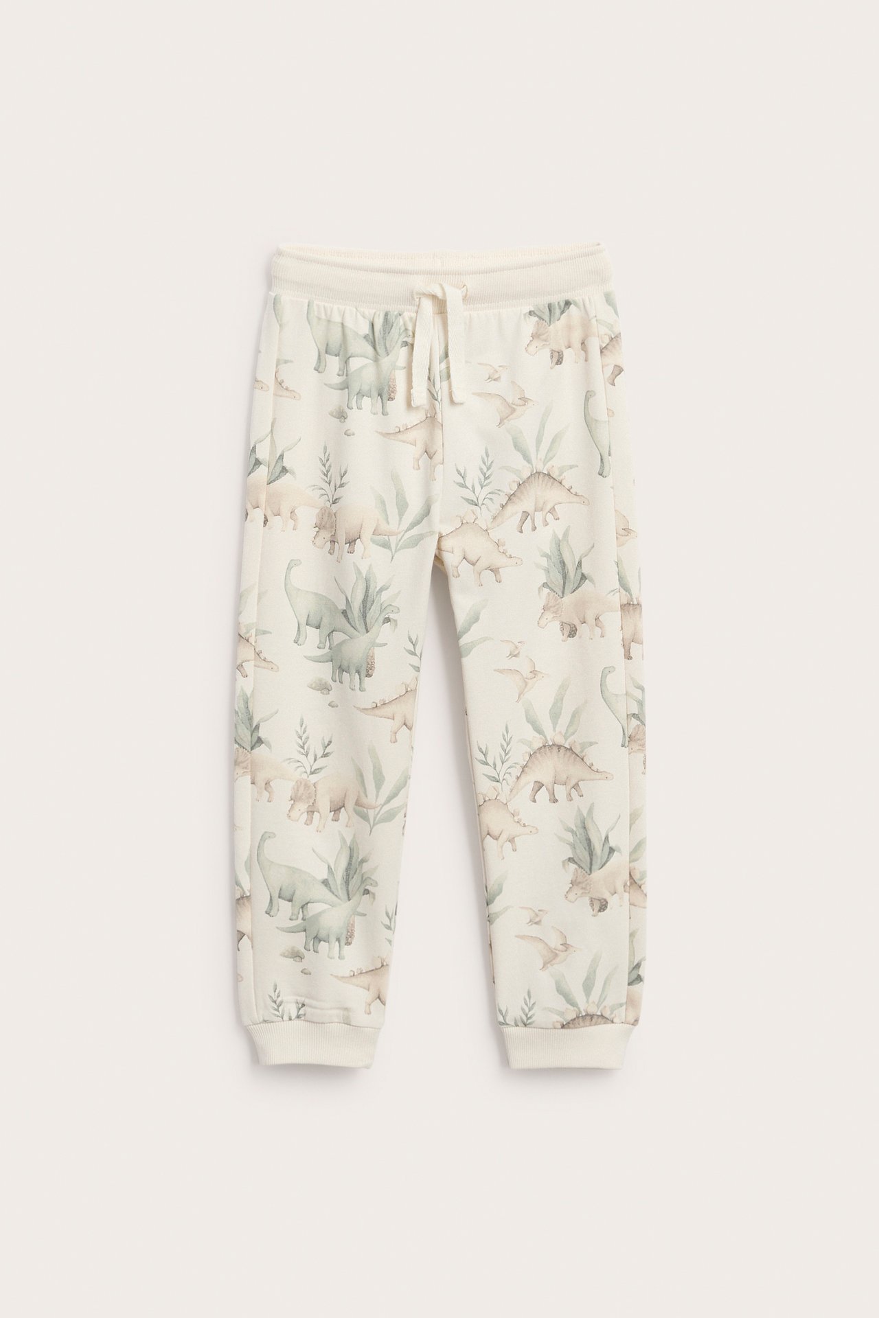 Vorderansicht von cremefarbenen Kinder-Jogginghosen mit Dinosaurier-Print, Kordelzug und Bündchen.