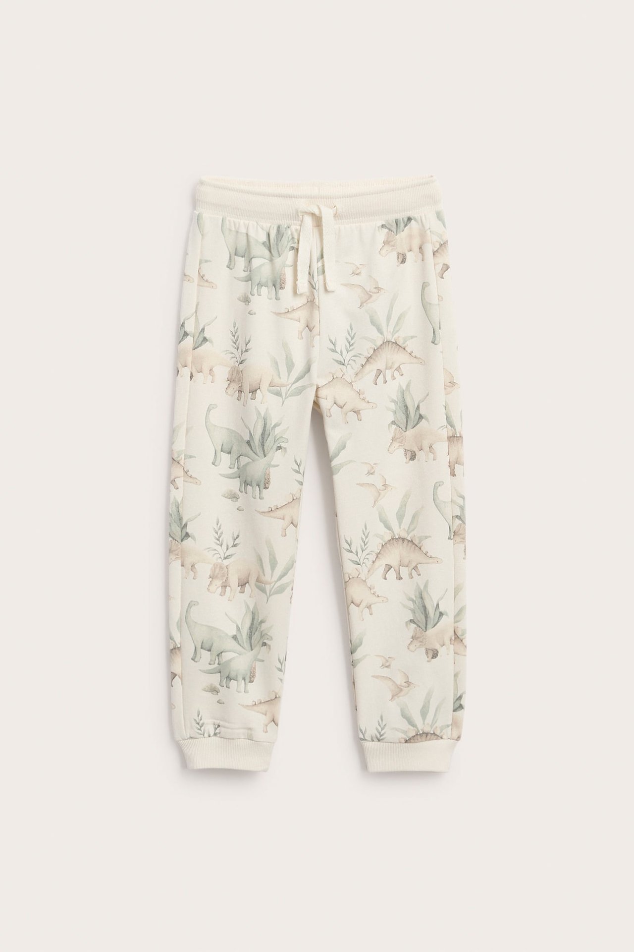 Vorderansicht von cremefarbenen Kinder-Jogginghosen mit Dinosaurier-Print, Kordelzug und Bündchen.