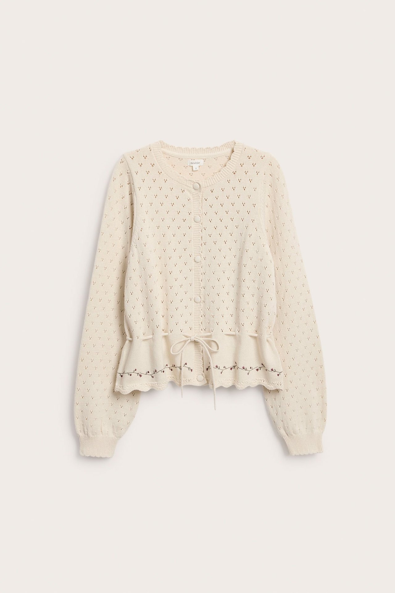 Vorderansicht einer cremefarbenen Strickjacke mit Knöpfen, Lochmuster, Blumenstickerei und Kordelzug.