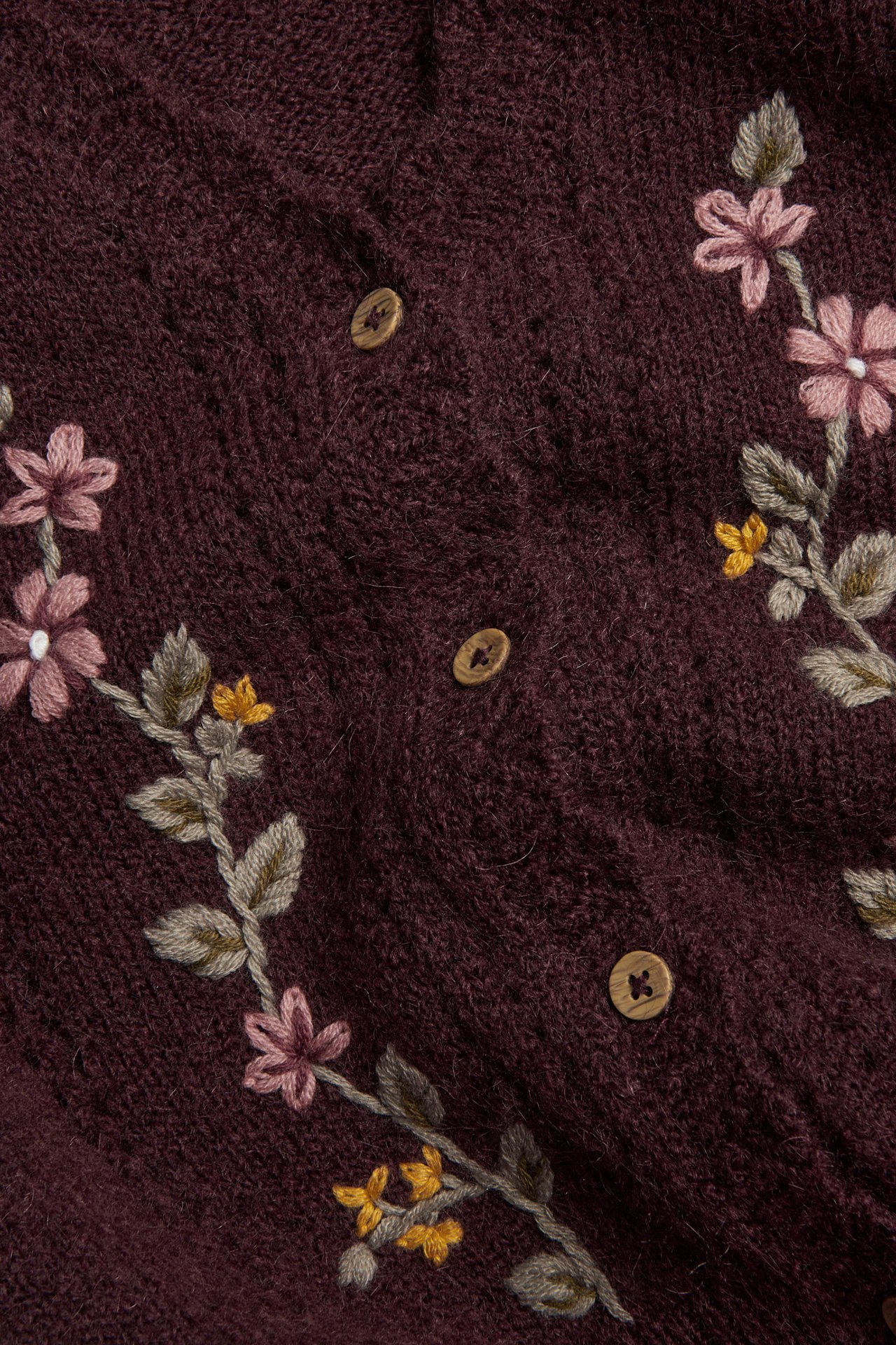 Nahaufnahme eines bordeauxfarbenen Strickcardigans mit Blumenstickerei und Holzknöpfen.