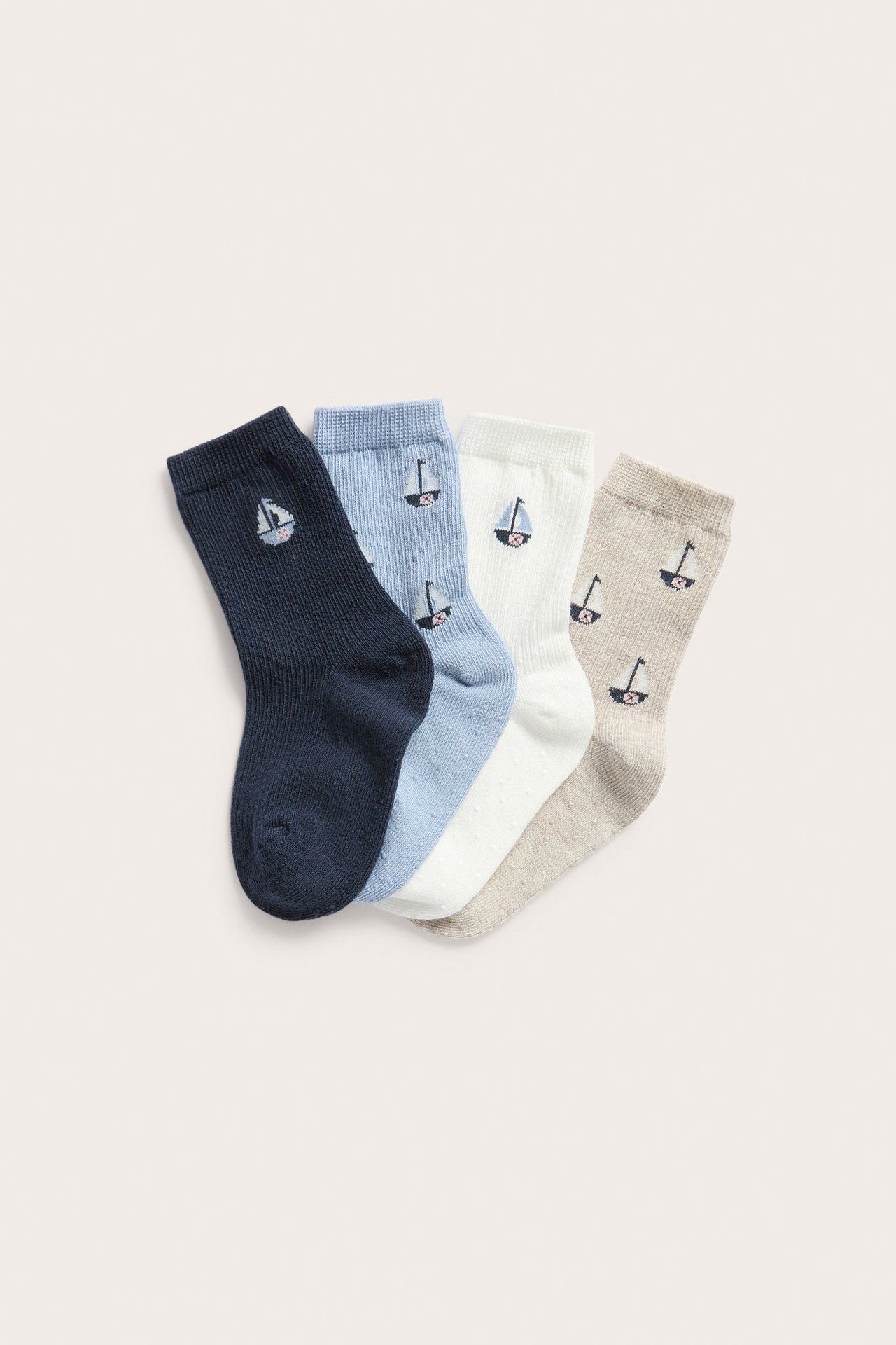 Top-down view of four pairs of cotton socks in navy, light blue, off-white, and beige, with sailboat motifs.