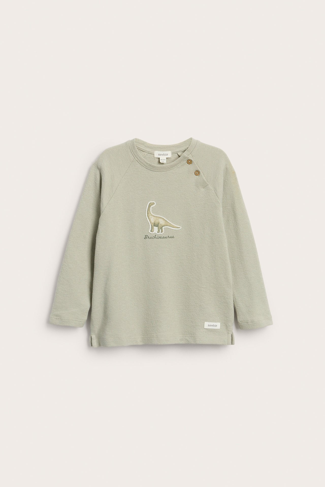 Front view of a light green structured jersey long-sleeved top with a Brachiosaurus dinosaur application and shoulder buttons.