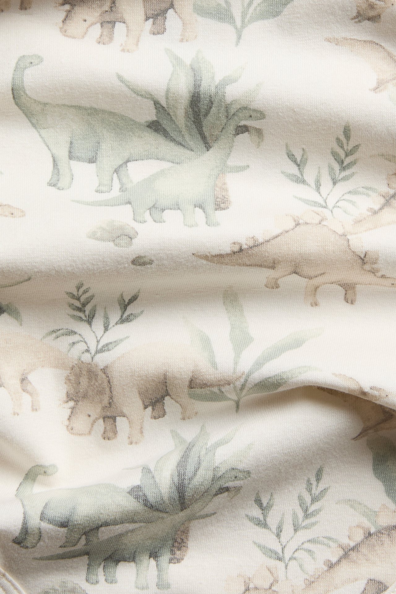 Close-up of cream textile with a green dinosaur and plant print.