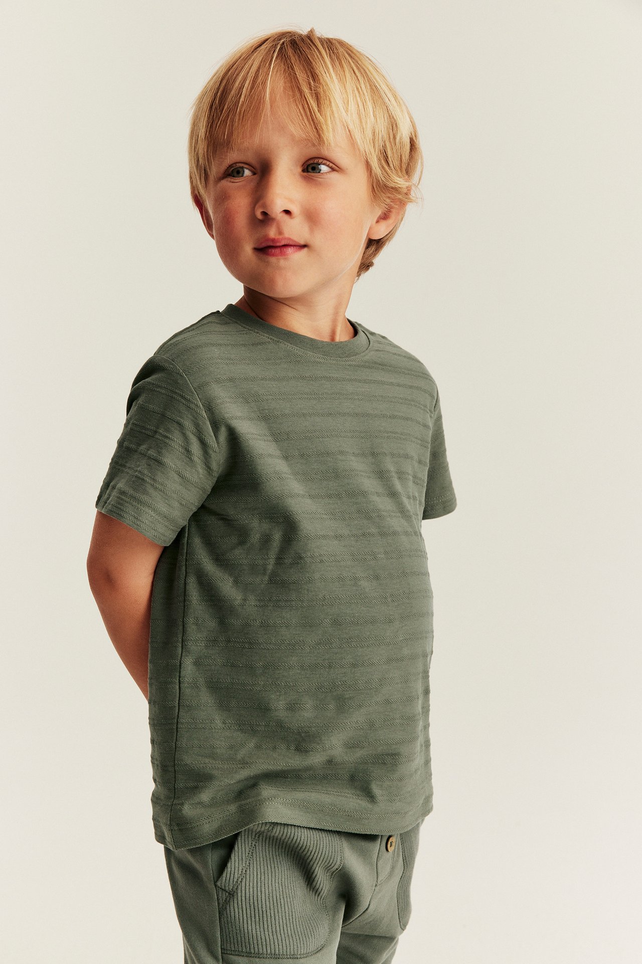 Front view of a kid wearing a green striped short-sleeved t-shirt and green ribbed sweatpants.